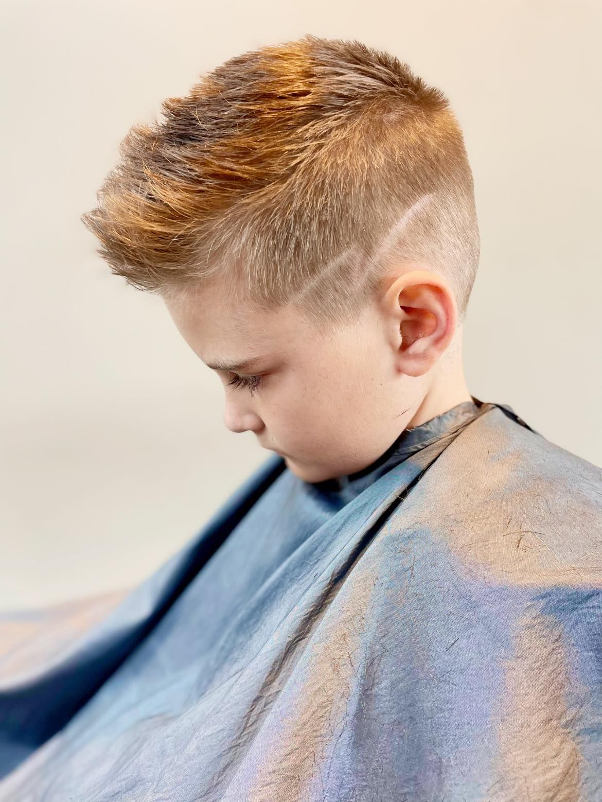 Side-view portrait of a child with short blond hair wearing a blue barber cape.