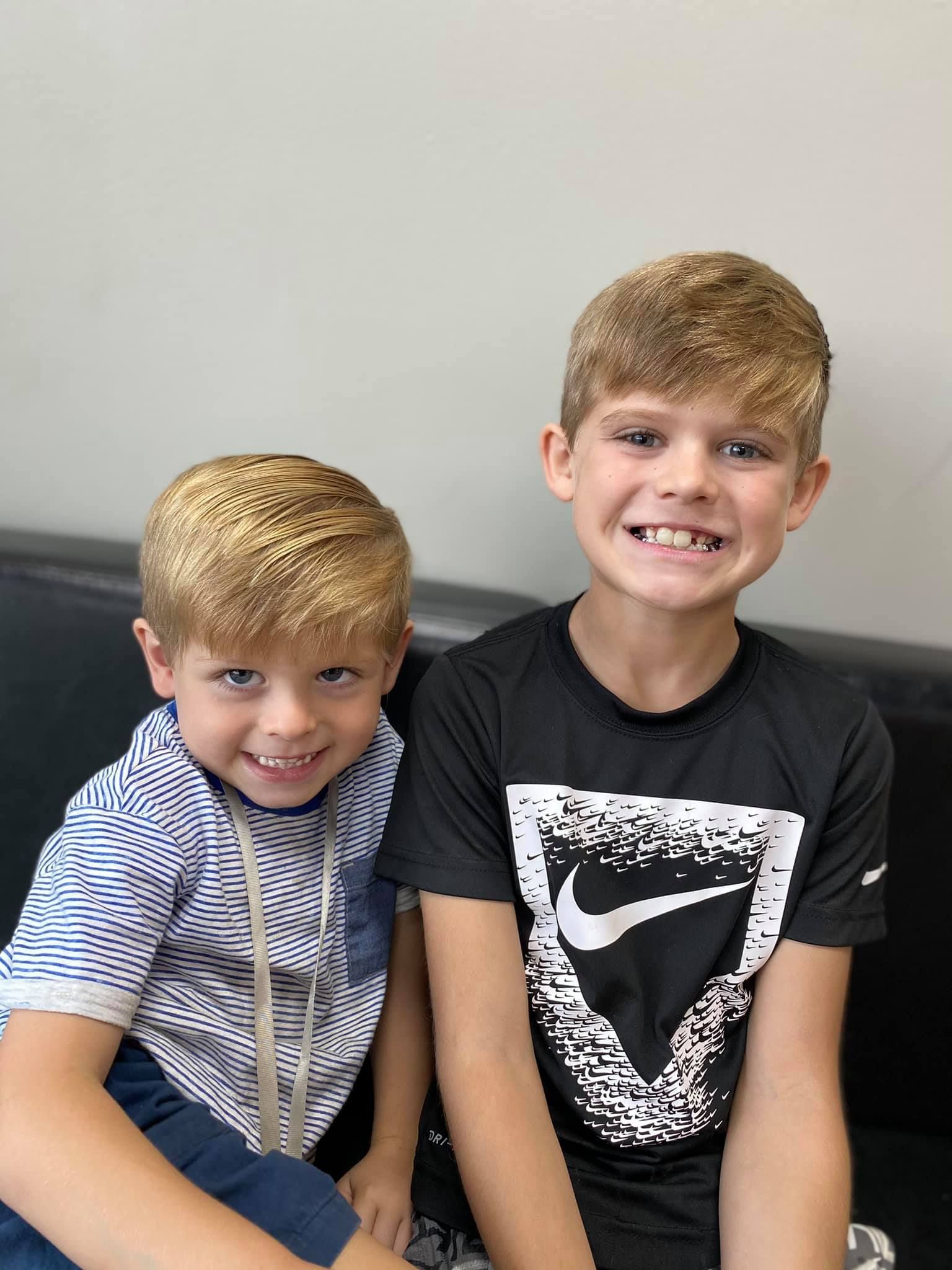 Two smiling children sitting on a couch, one in a striped shirt and one in a black graphic T-shirt.