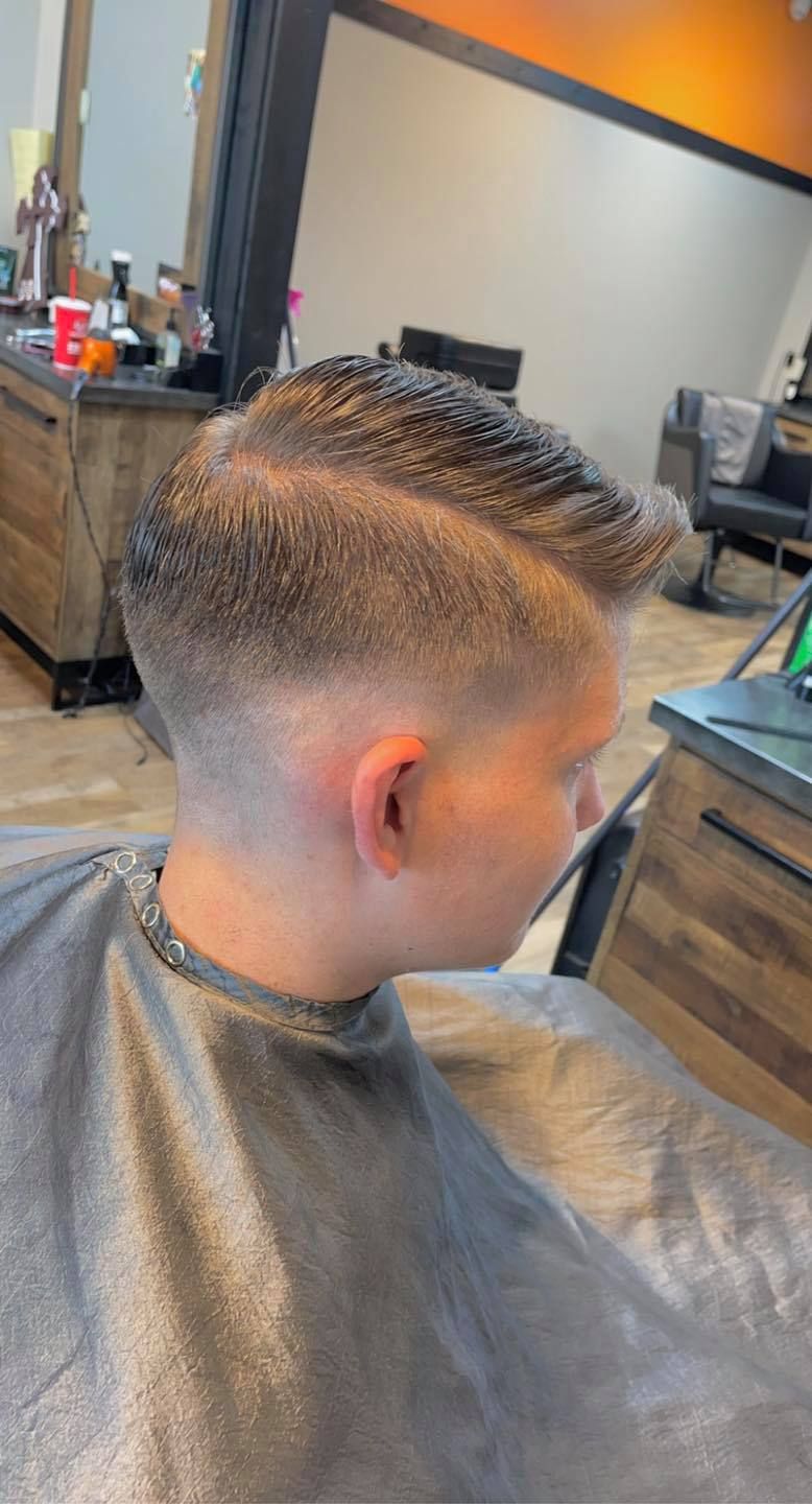 Boy with a faded mohawk haircut seated in a barbershop chair, seen from the side.