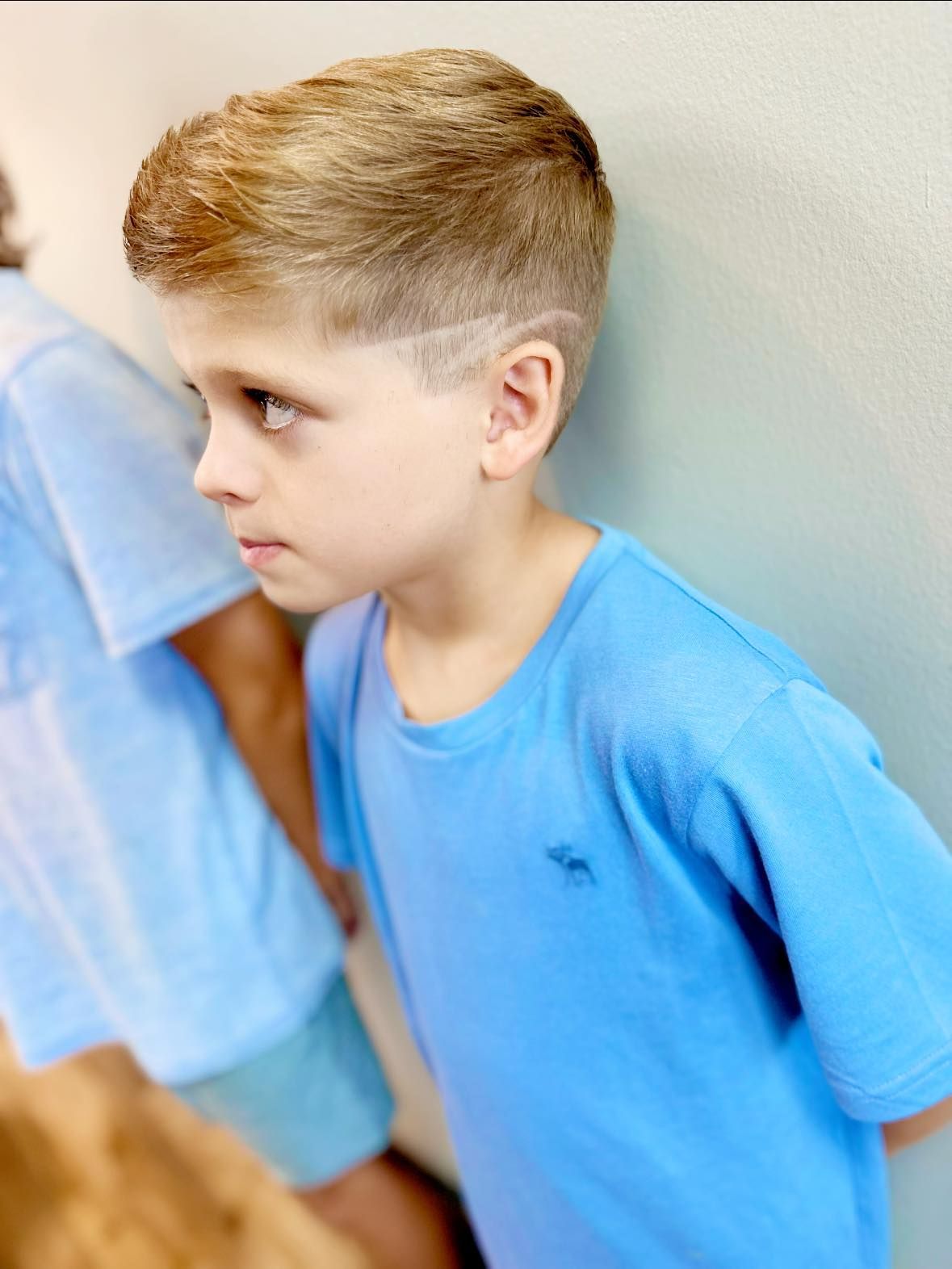 Boy in a blue shirt standing against a wall, looking to the side.