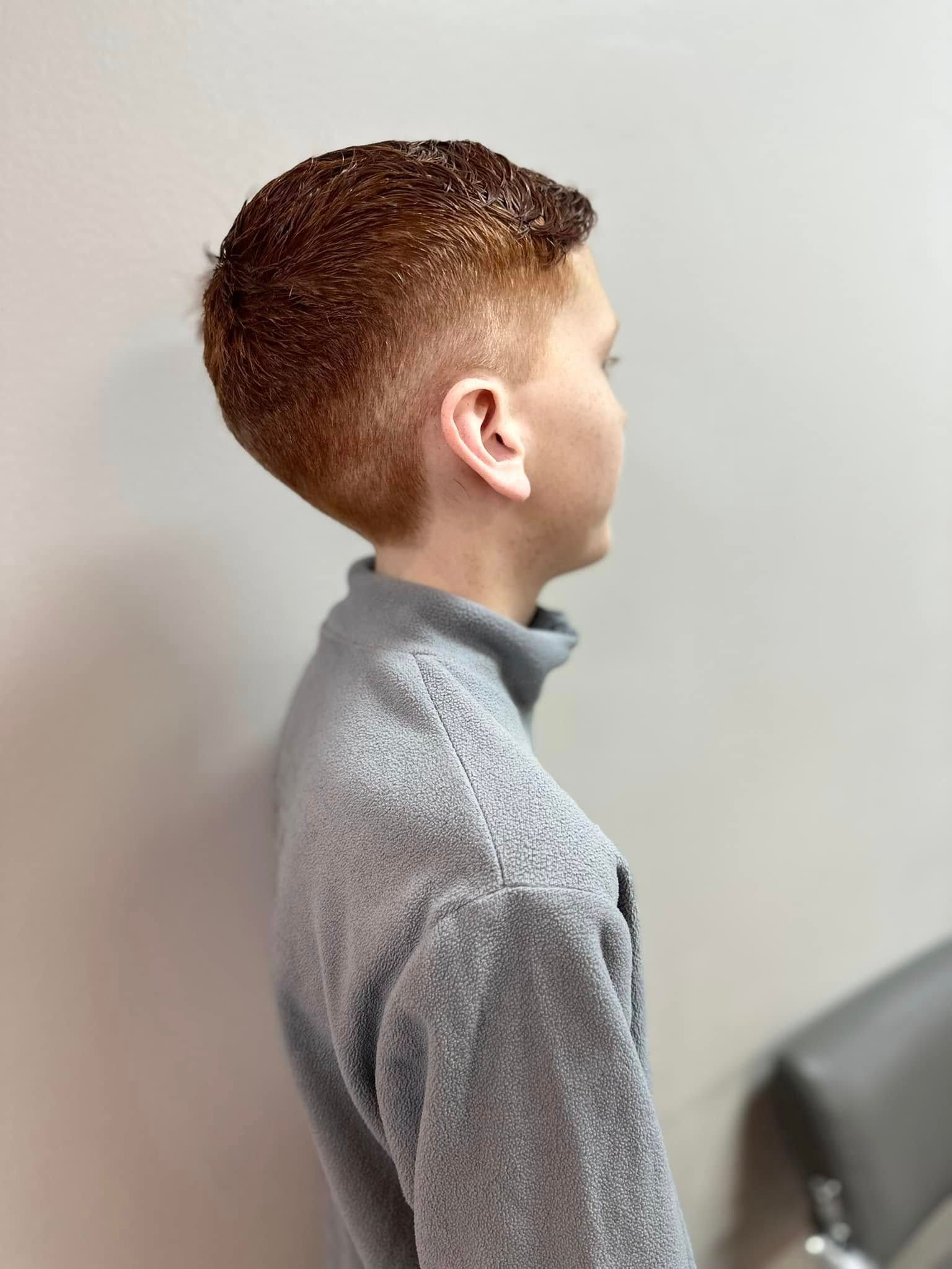 Side view of a person with a short brown haircut wearing a gray turtleneck sweater against a plain wall