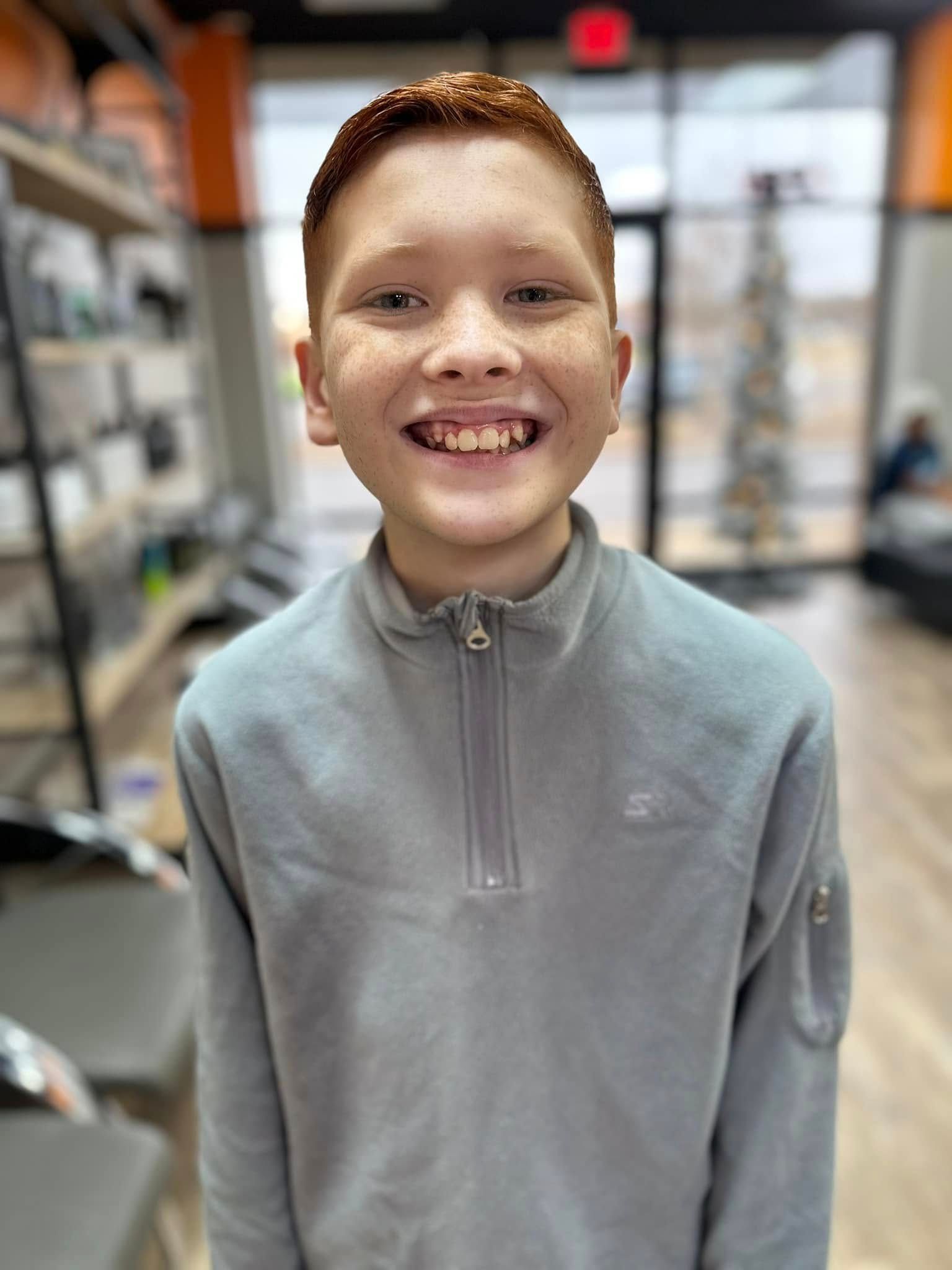 Smiling child in a gray zip-up pullover standing indoors with a blurred store-like background