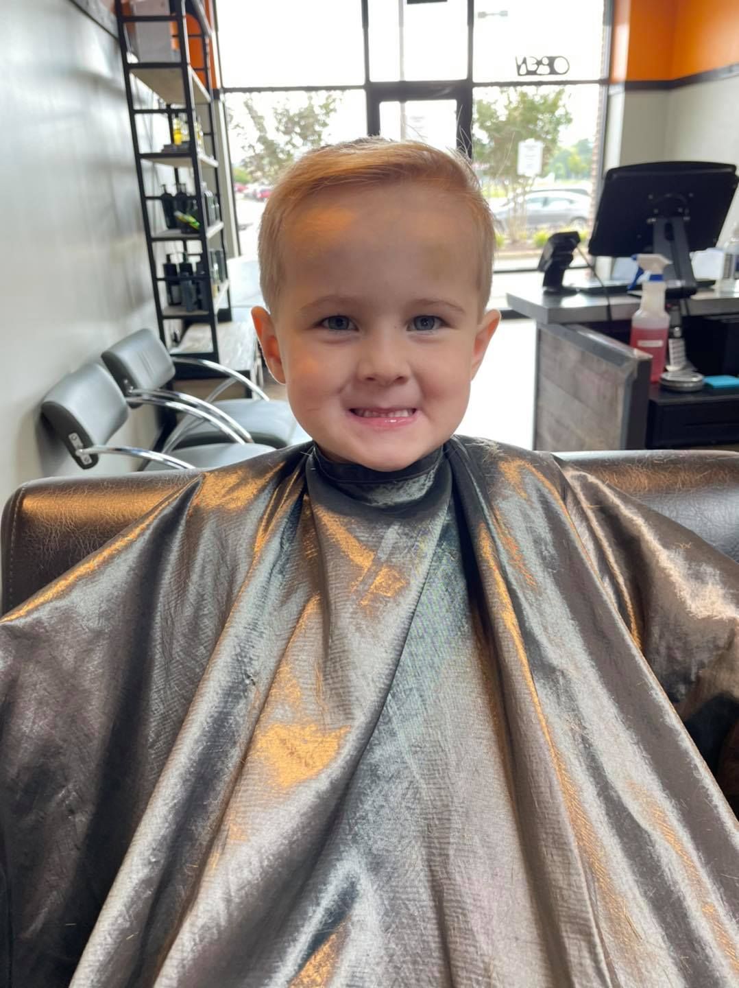 Smiling child in a silver salon cape seated in a bright hair salon