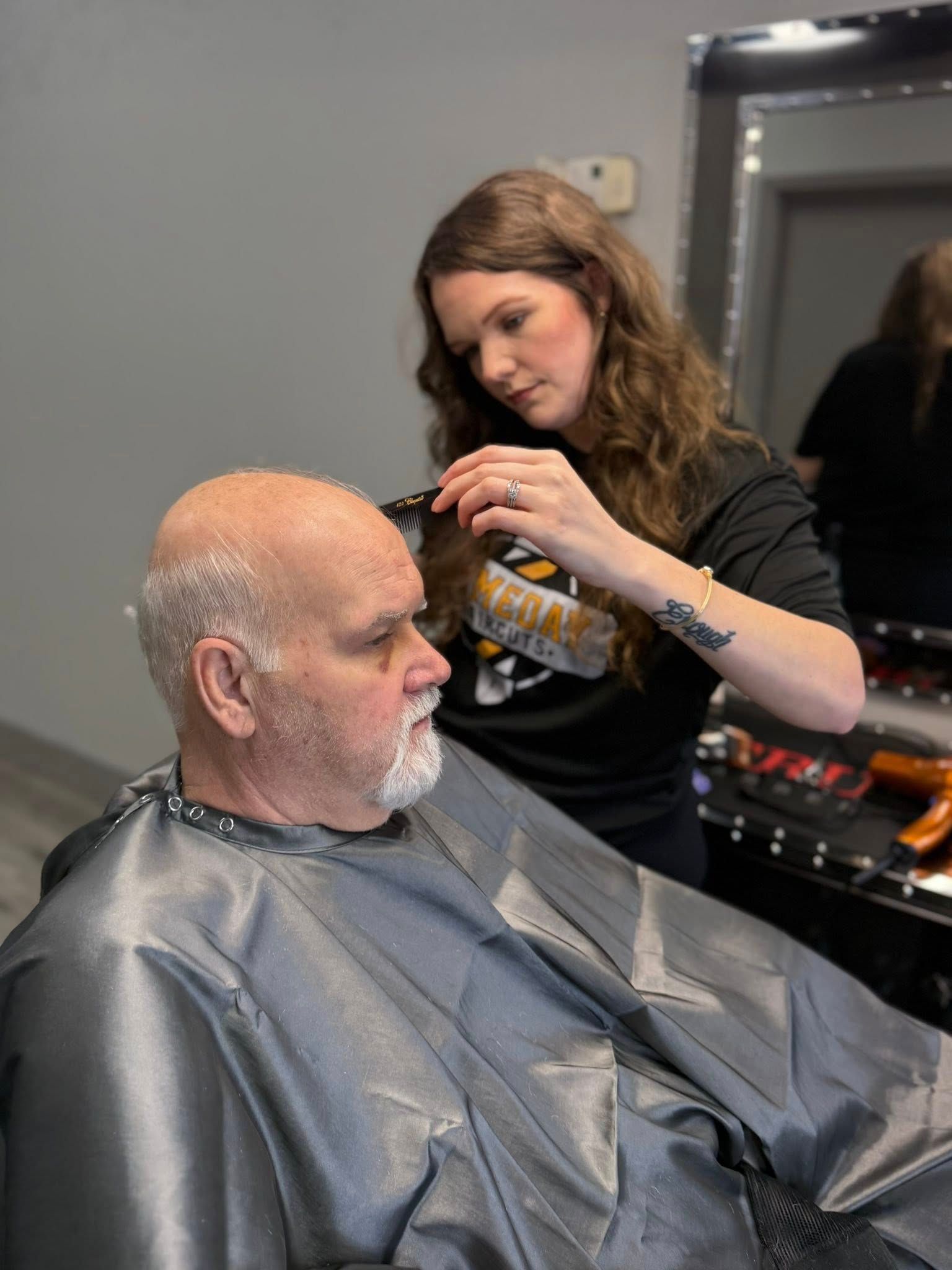 Hair stylist cutting hair of a man in a salon. The stylist is using a comb and scissors.