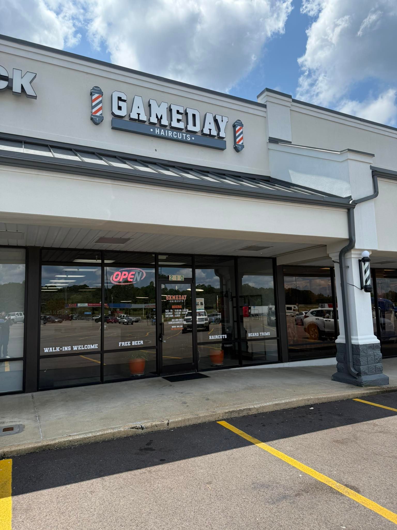 Exterior of a barber shop called "Game Day" with glass doors and windows under a bright sky.