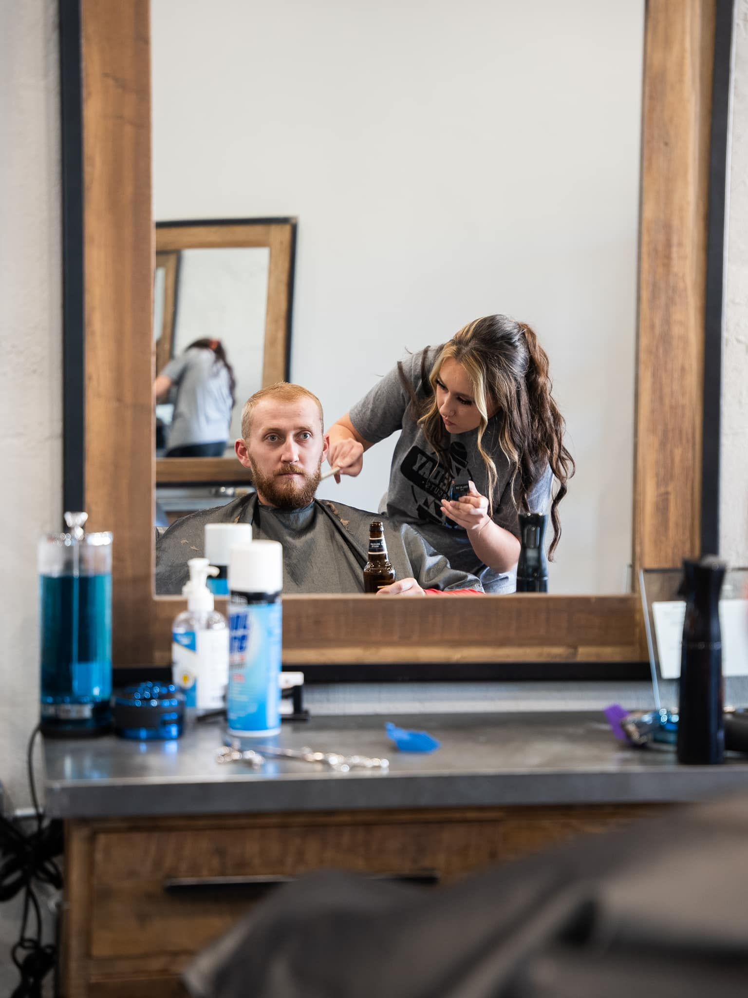 Barber trimming a client’s hair in a mirror-lit salon, with grooming products on the counter.