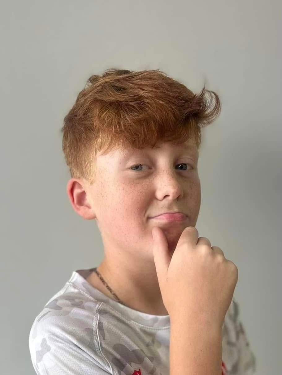 Person with short reddish hair poses thoughtfully against a plain light gray background.
