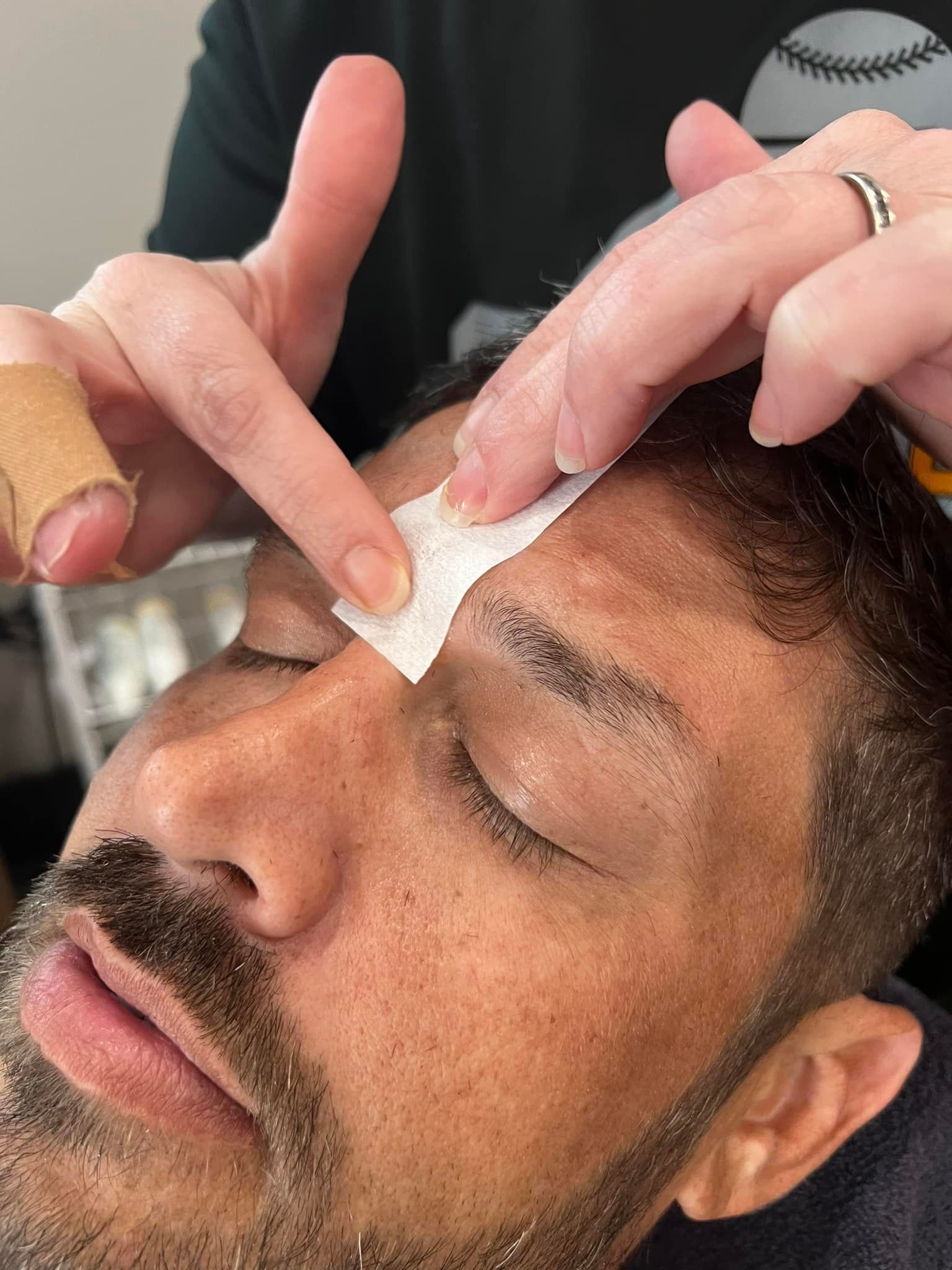 Person having eyebrow wax; esthetician pressing strip to forehead.