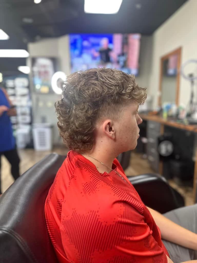 Person in a red cape sits in a barbershop chair, shown in side profile.
