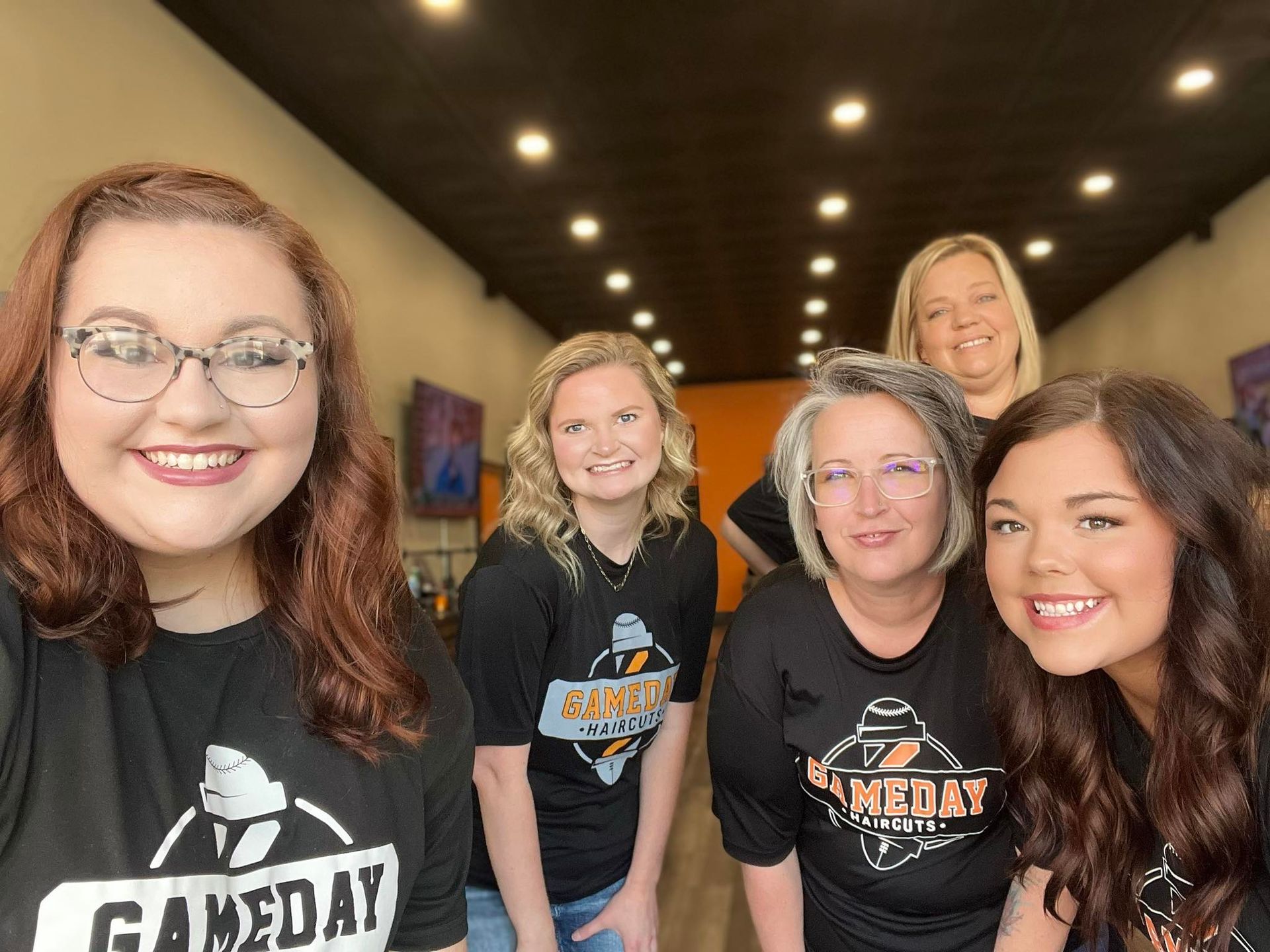 Five people in black "GAMEDAY" shirts smile inside a store with orange and black accents.