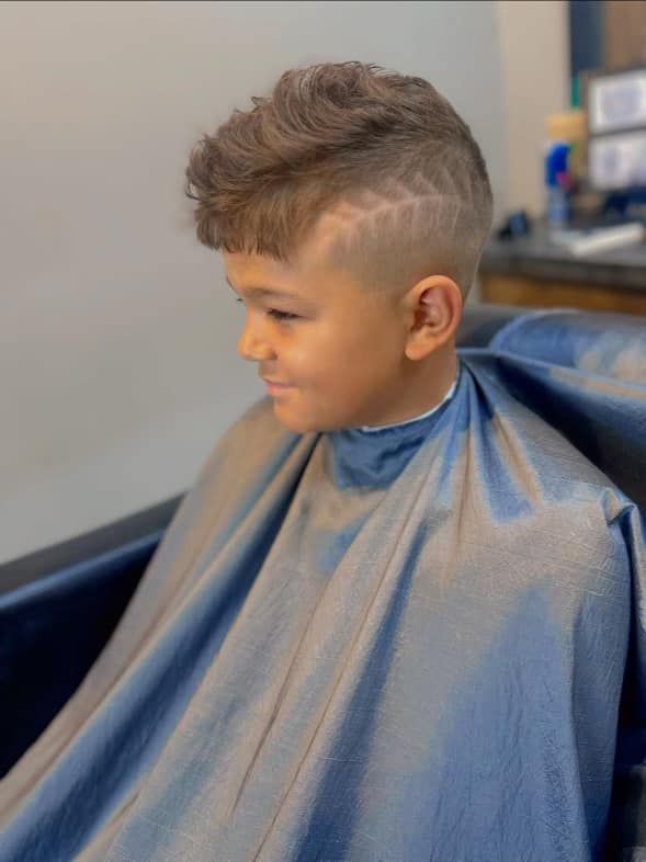 Child with a stylish haircut wearing a gray barber cape in a salon chair