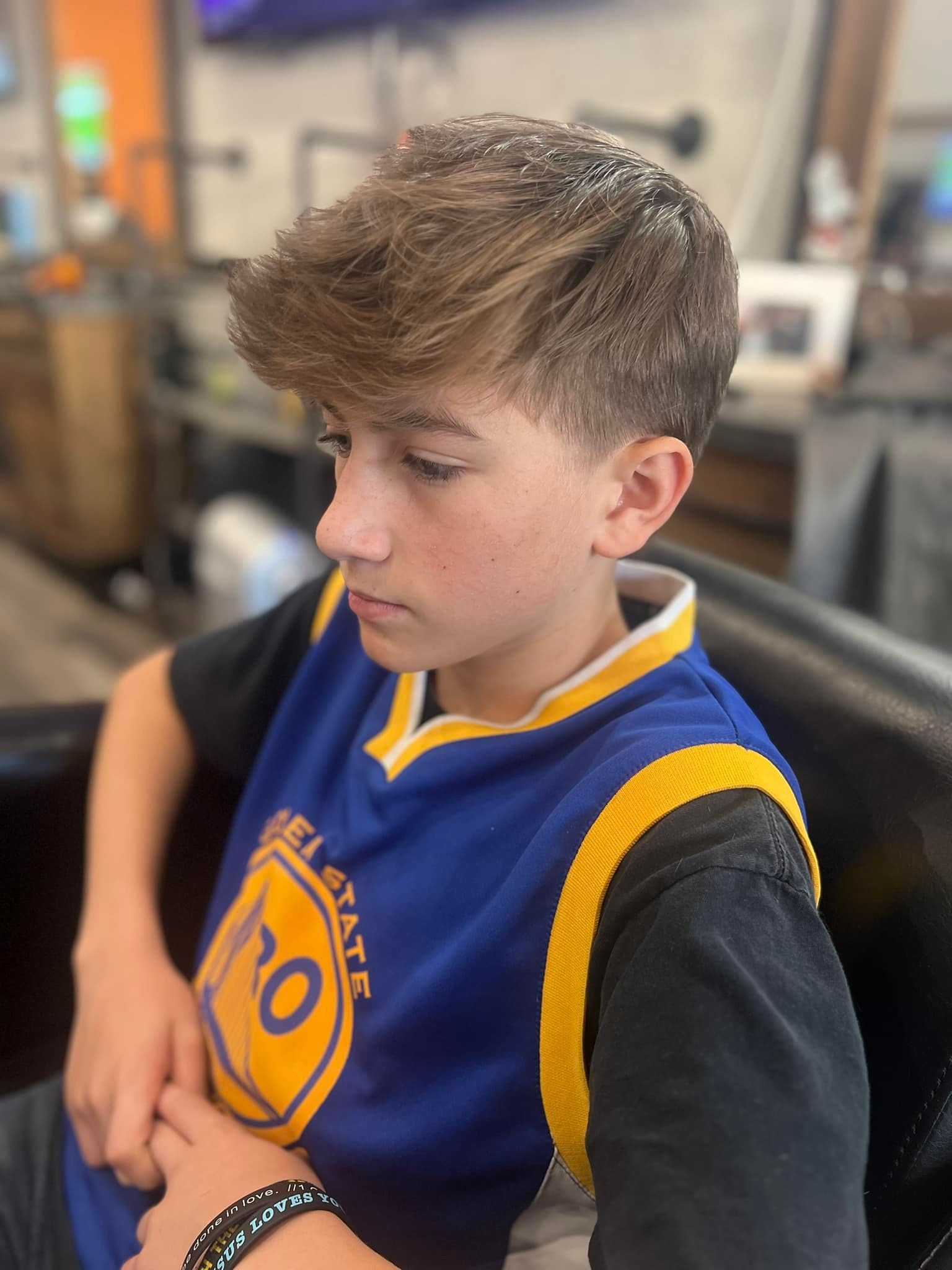 Teen in a blue-and-yellow sports jersey sits in a chair, looking down in a room.