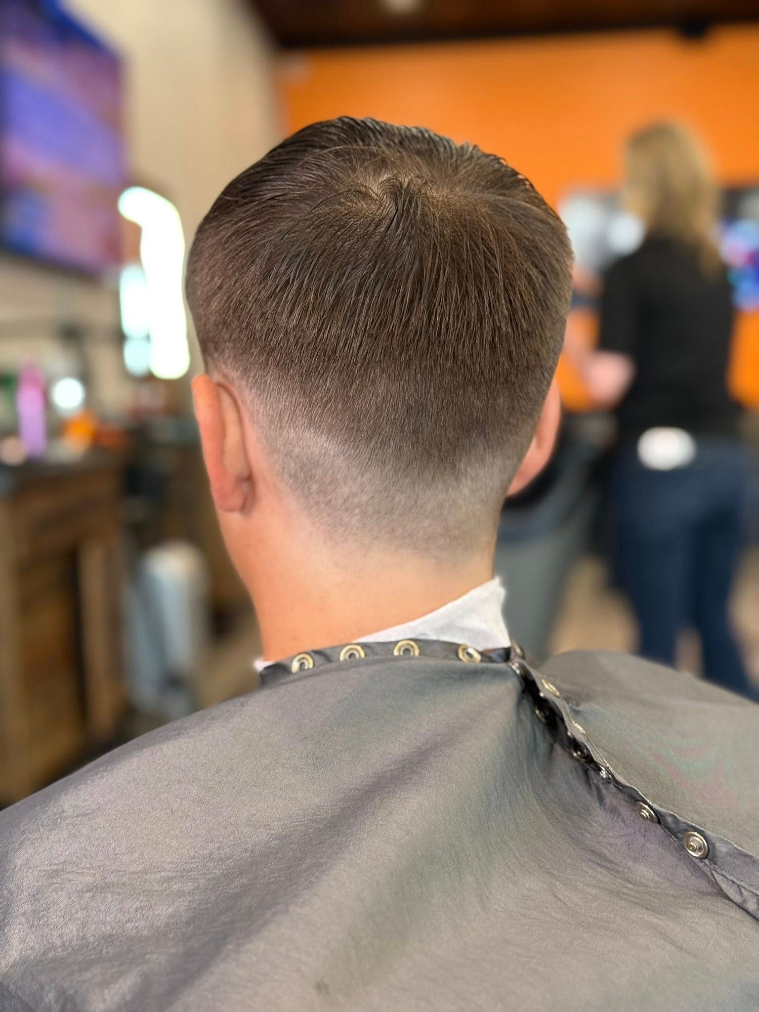 Back of a short fade haircut at a barbershop, cape draped over shoulders