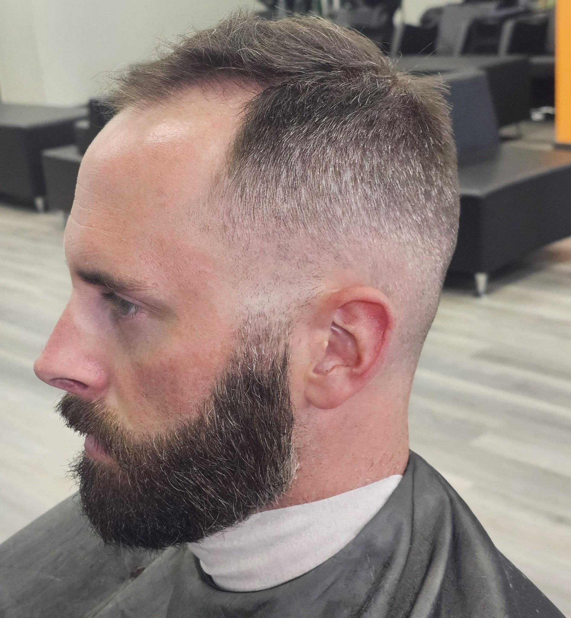 Side-profile of a man with a faded haircut and full beard in a barbershop chair