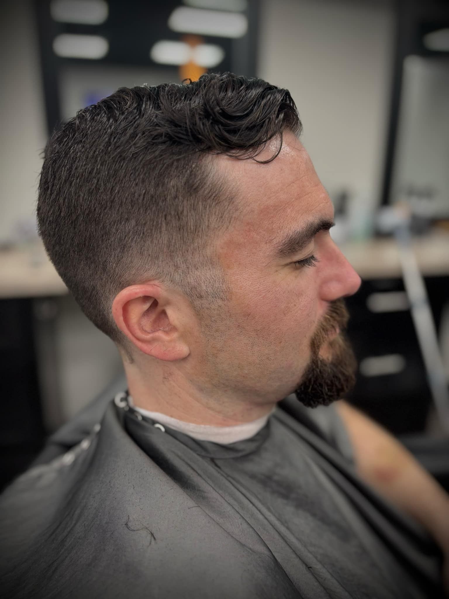 Man with a faded haircut and trimmed beard sitting in a barber chair during a haircut