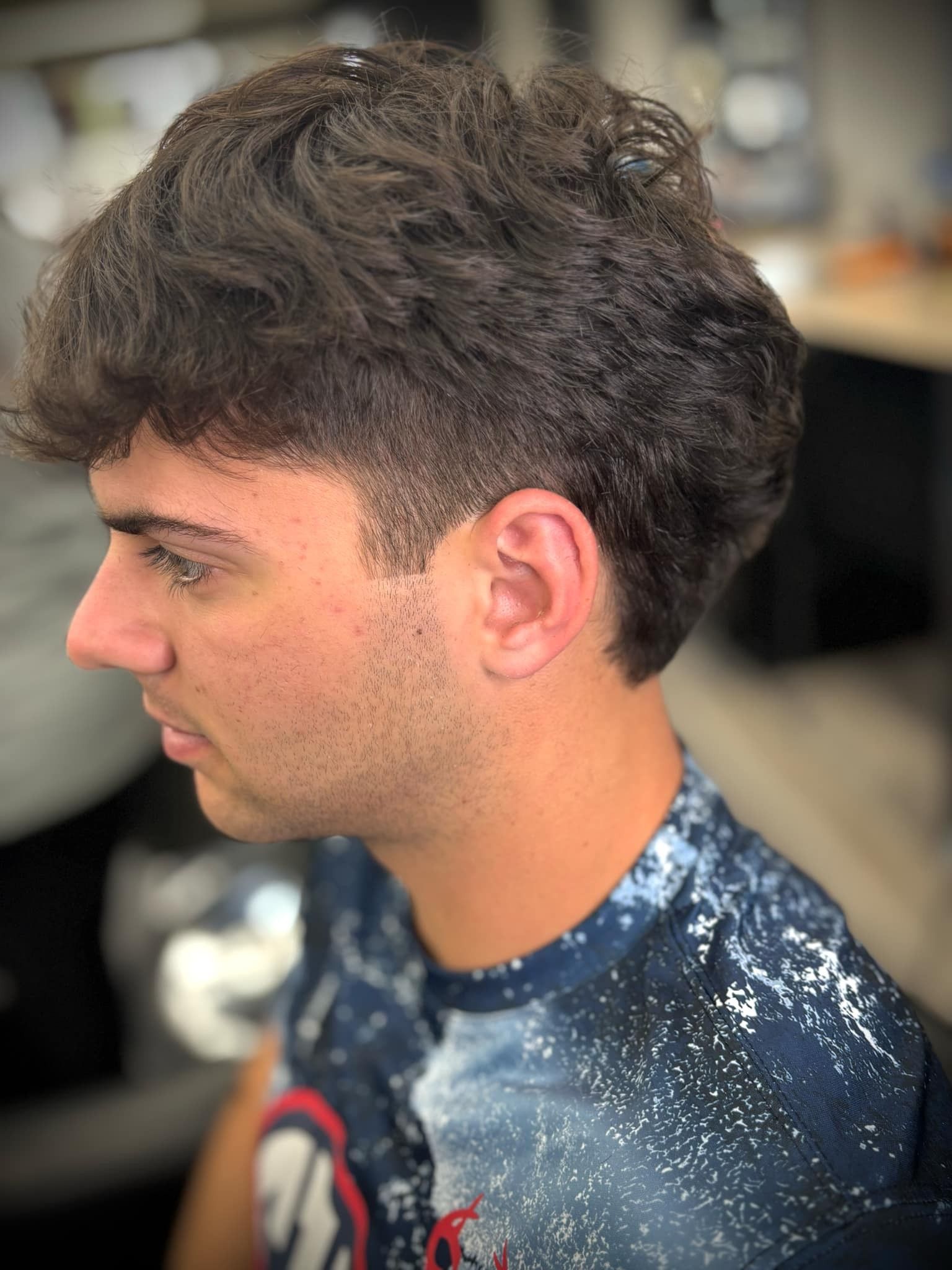 Side profile of a person with curly hair wearing a dark blue speckled shirt in a salon setting