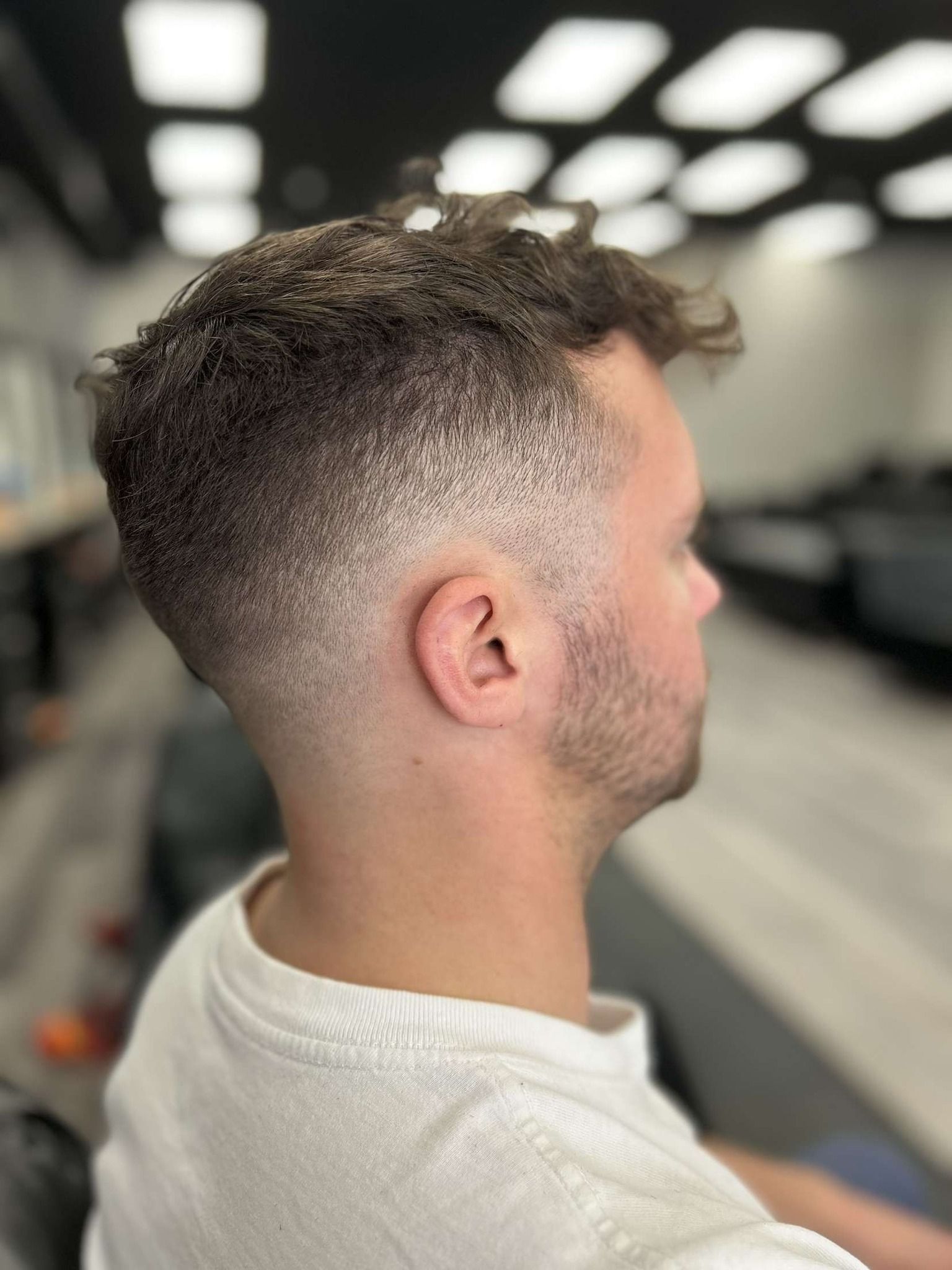 Side profile of a man with a faded curly haircut in a barber shop mirror.
