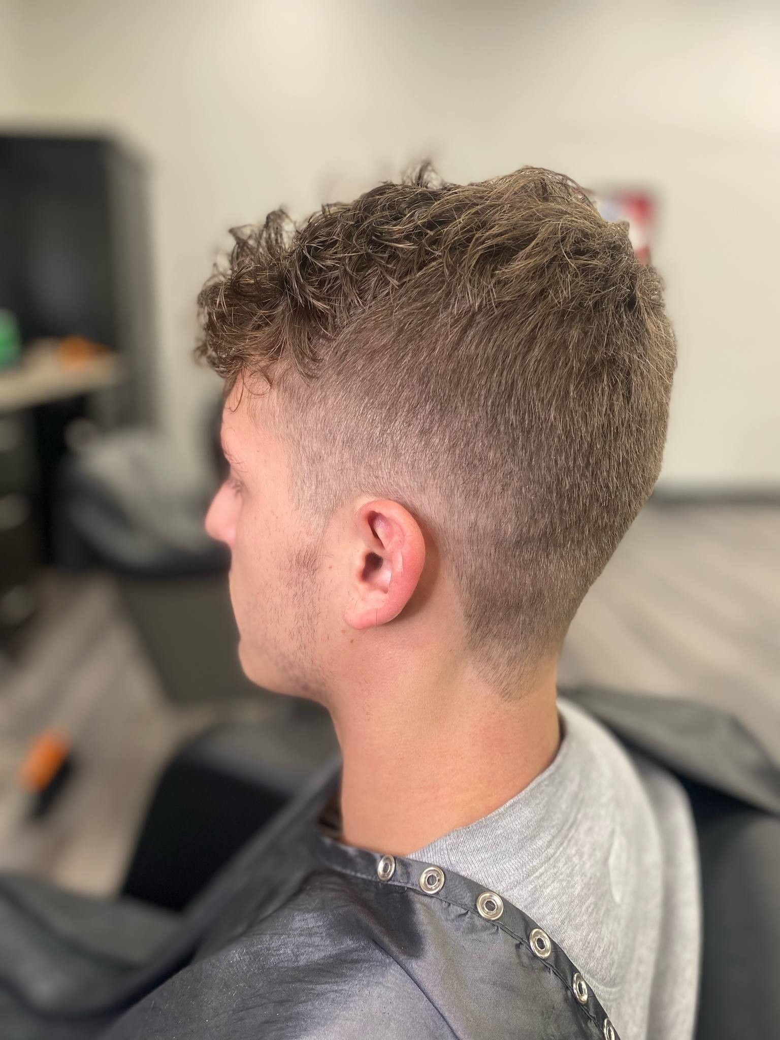 Side profile of a short curly-haired person in a barbershop, showing a faded haircut.