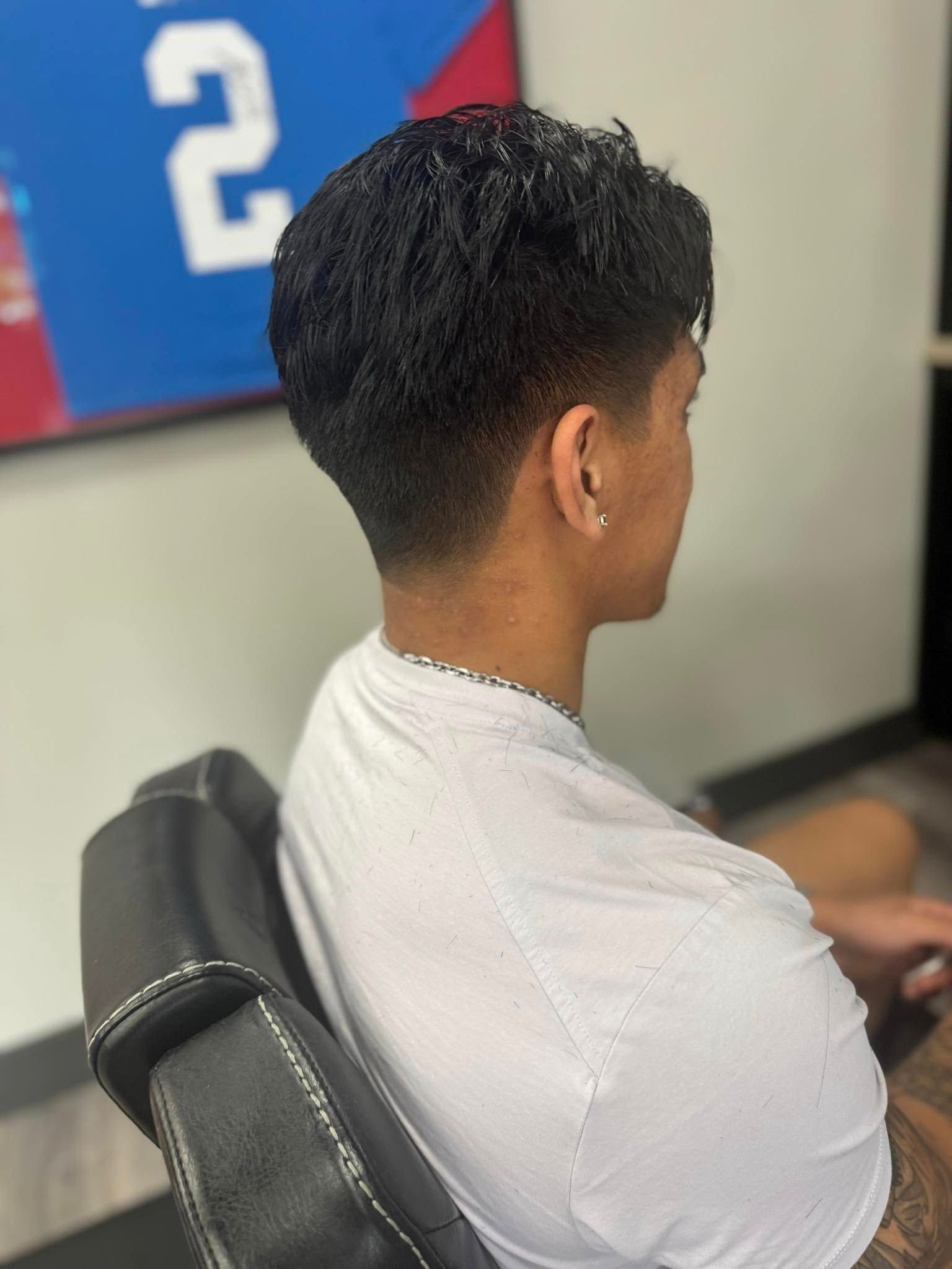 Person seated in a chair, viewed from behind, wearing a light gray shirt in a salon-like setting.