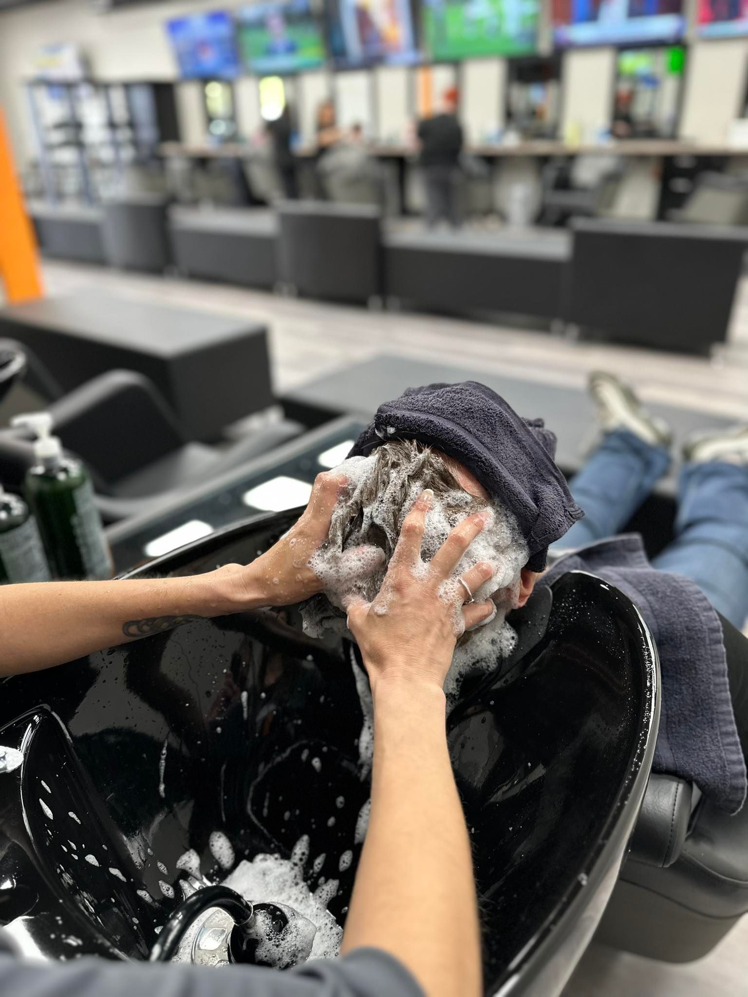 Person washing hair in a salon sink, with white suds and a blurred salon background