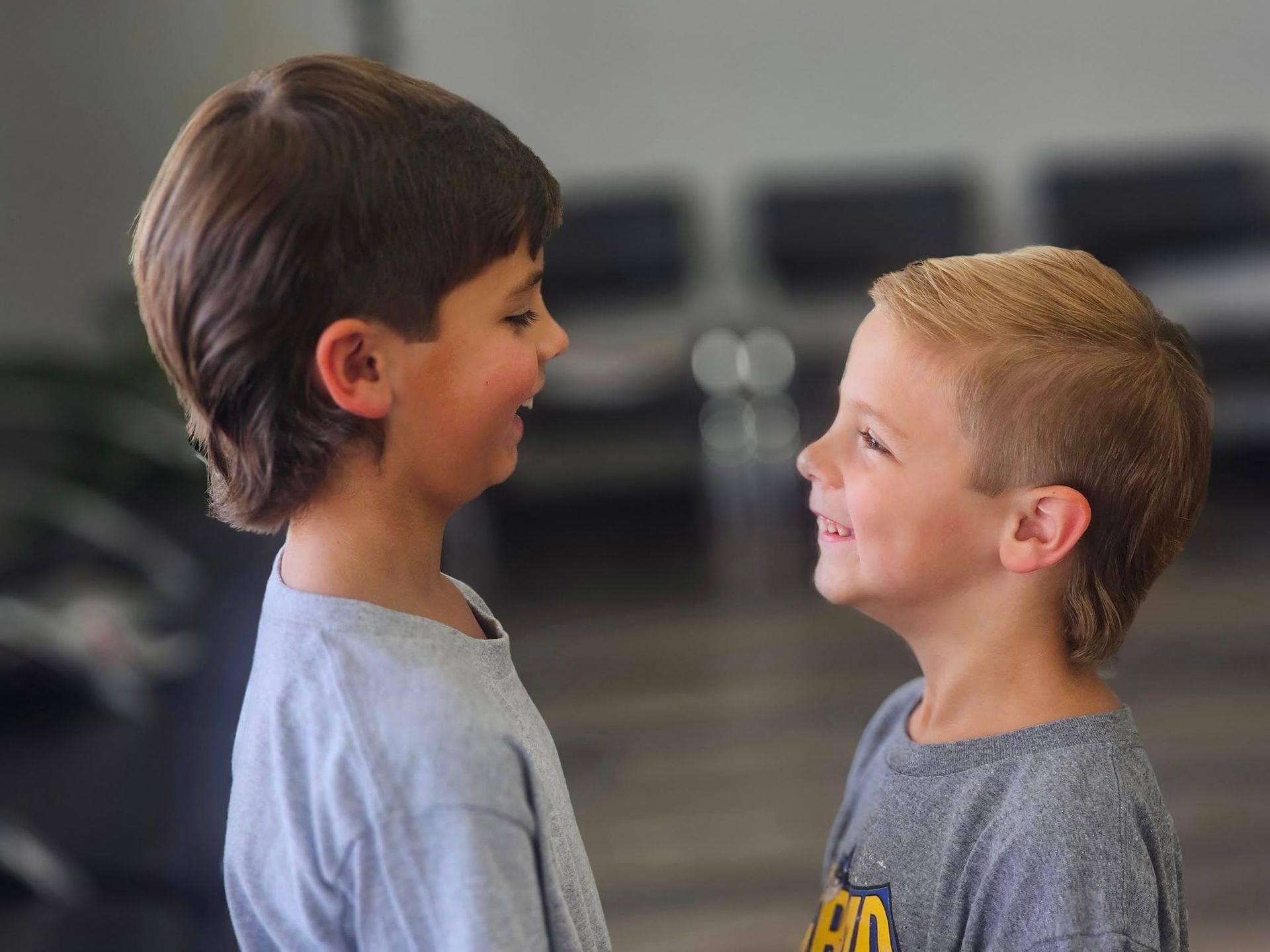 Two children facing each other and smiling in a blurred indoor setting