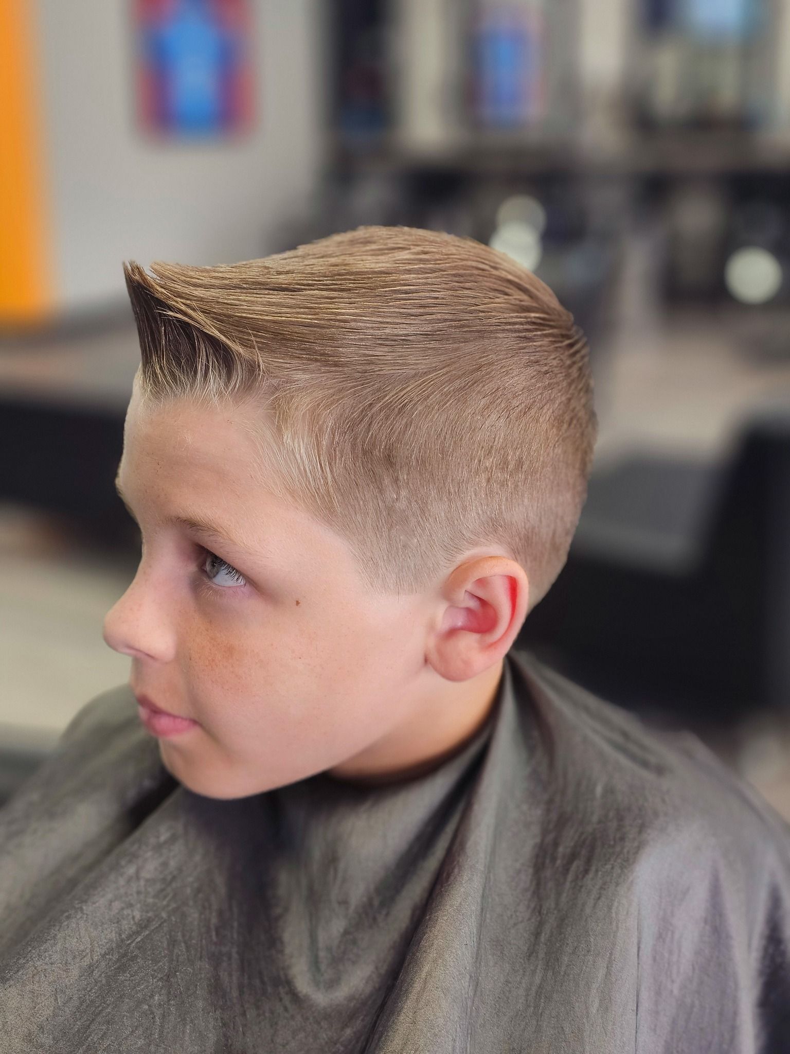 Close-up of a child with a short fade haircut in a barber chair, looking left in a salon.