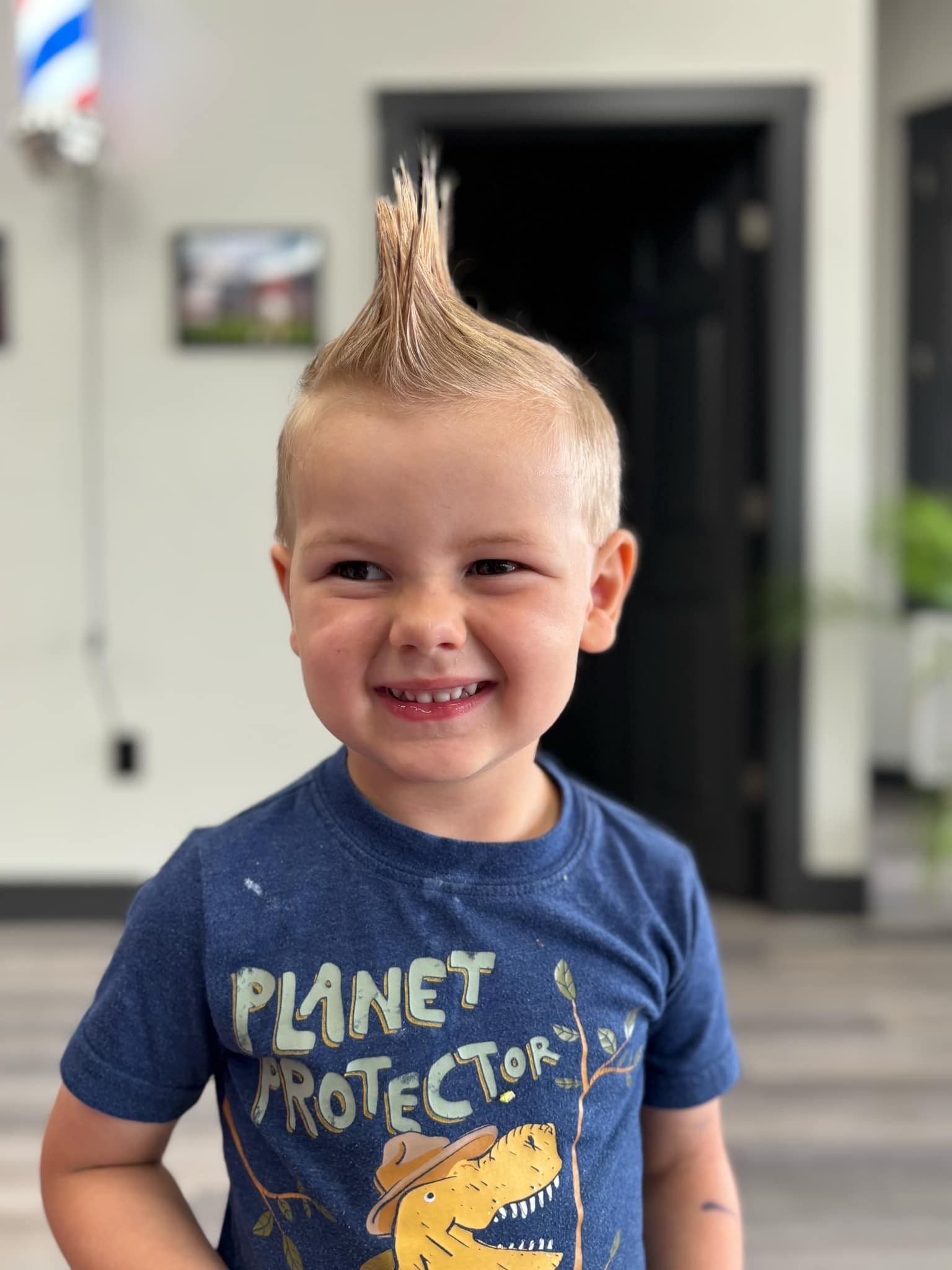 Smiling child with spiky blond hair wearing a blue Planet Protector shirt indoors
