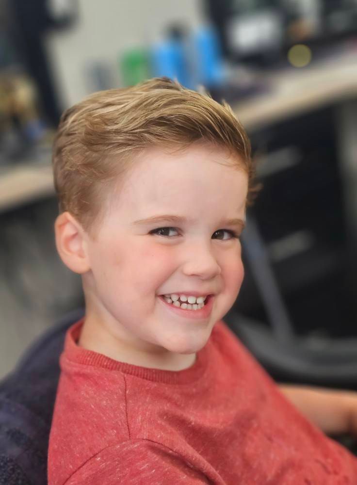 Smiling child in a red shirt sitting indoors with a blurred background