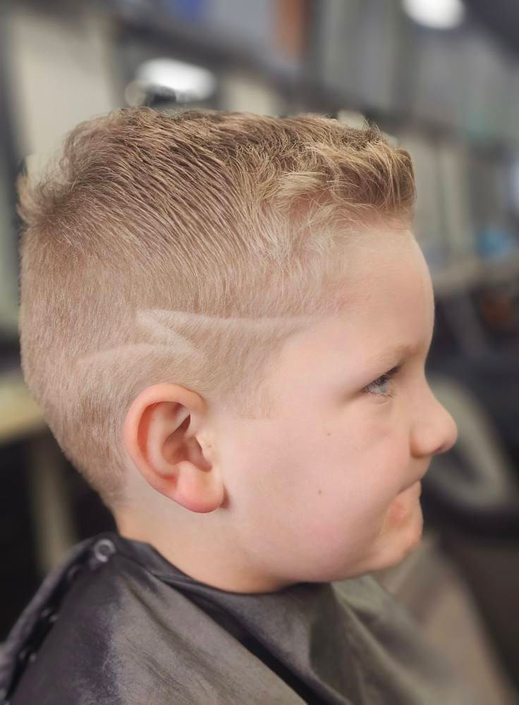 Side profile of a child with a short blond fade haircut in a barbershop chair