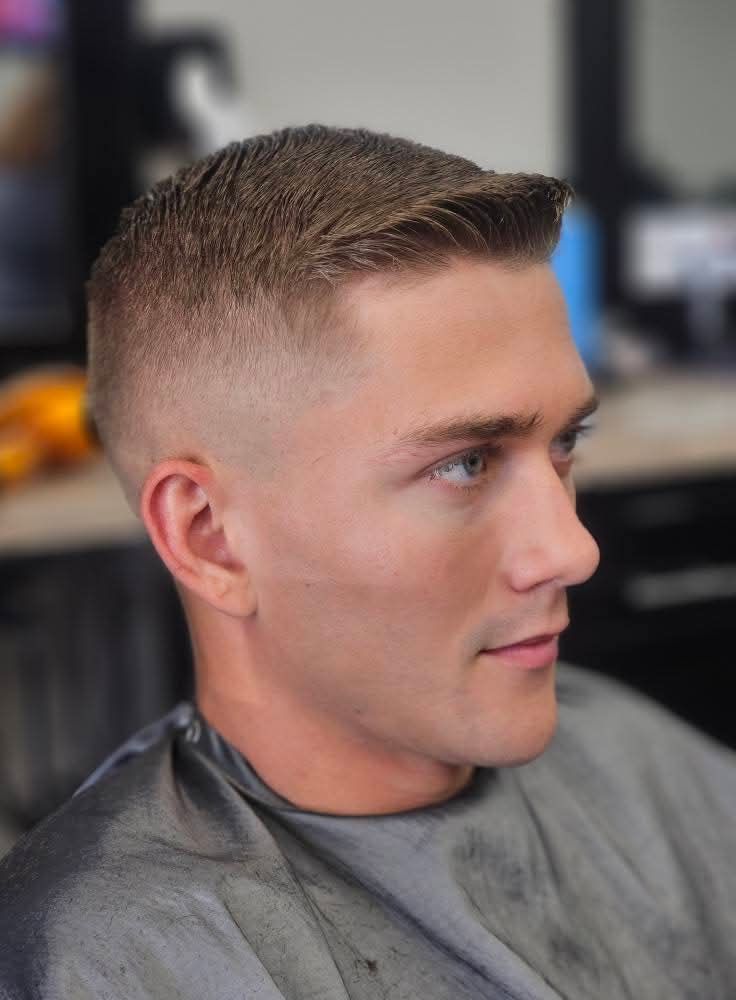 Close-up of a man with a short fade haircut, looking to the side in a barbershop chair