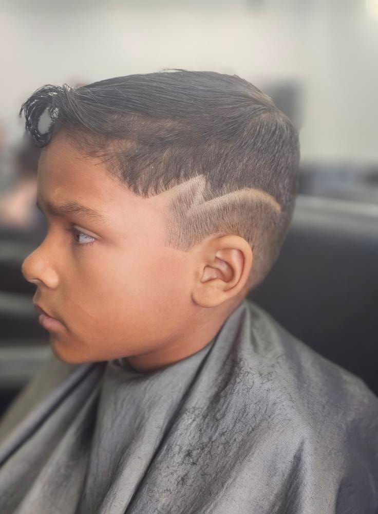 Side view of a child’s haircut with a shaved zigzag design, seated in a barber cape.