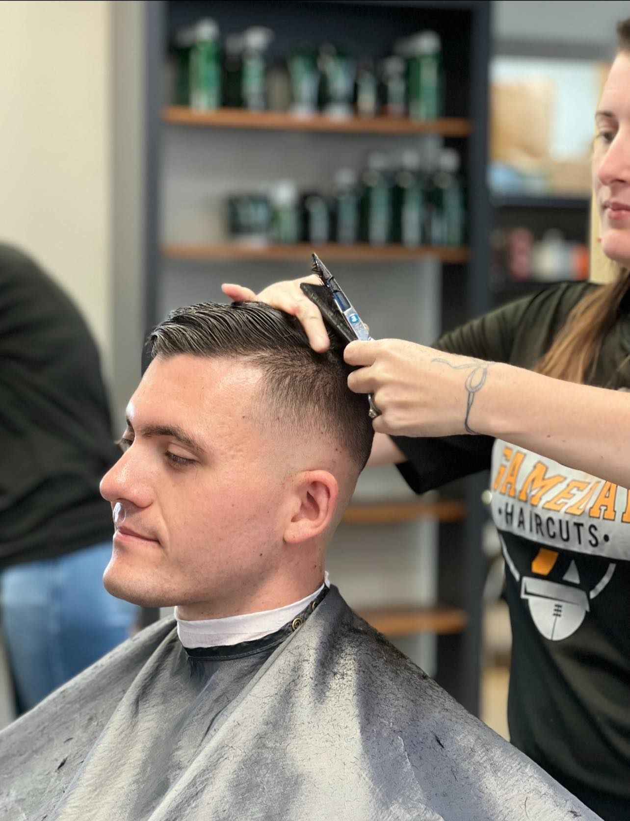 Barber trimming a man’s hair in a salon, with clippers and a cape.