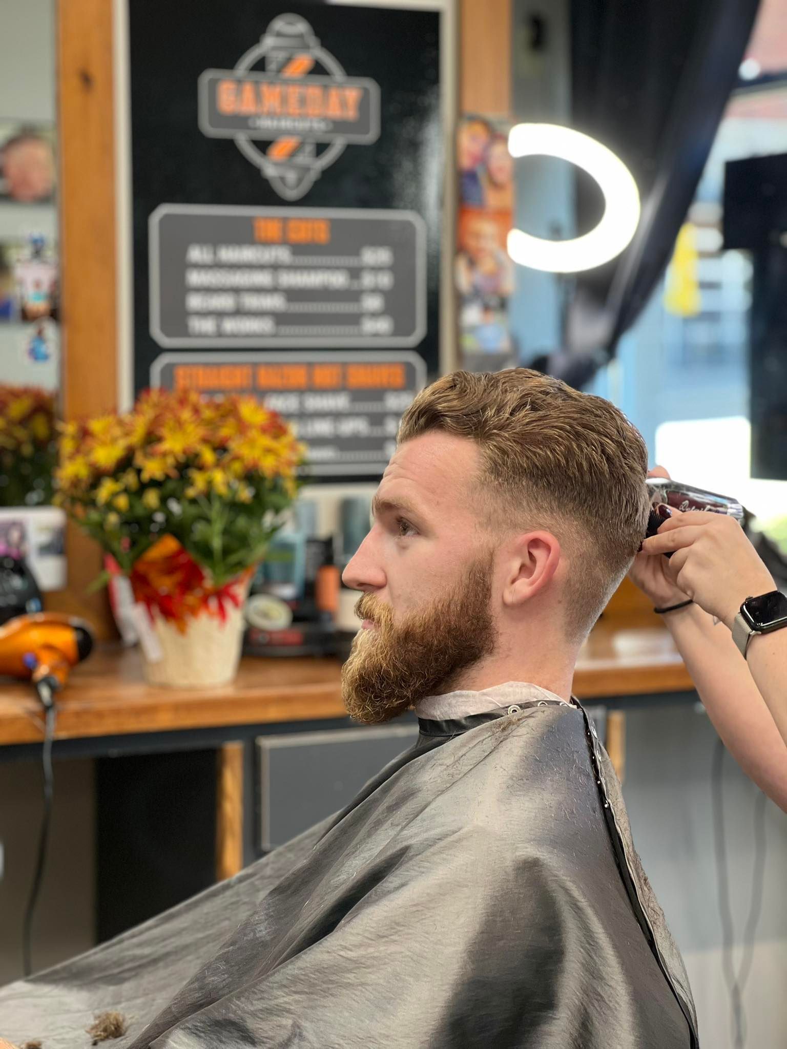 Man getting a haircut at a barbershop, with a barber trimming his hair.