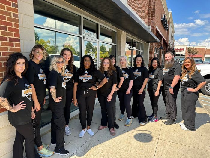 Group of people wearing black shirts and pants, posing outside a brick building on a sunny day.