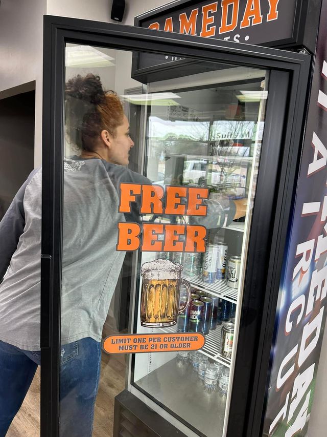 Woman reaching into a refrigerator labeled "Free Beer." Inside are various drinks.
