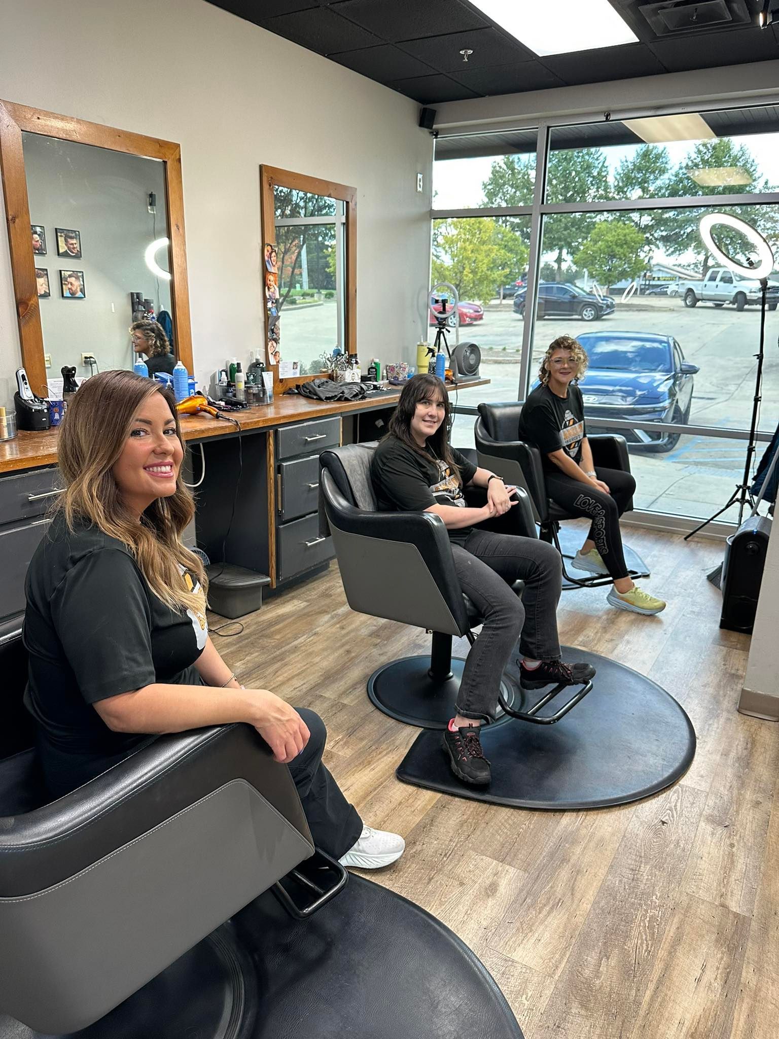 Three people seated in a hair salon. Two customers seated, one stylist. Smiling.