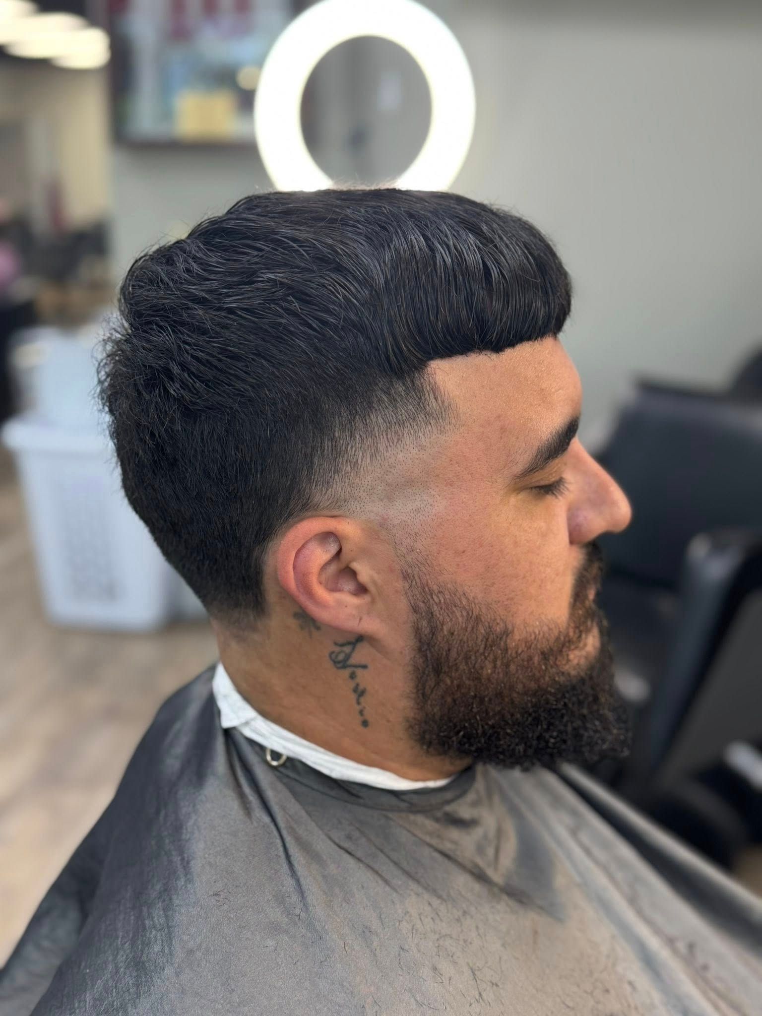 Man getting a fresh fade haircut in a barbershop, with a ring light glowing behind him