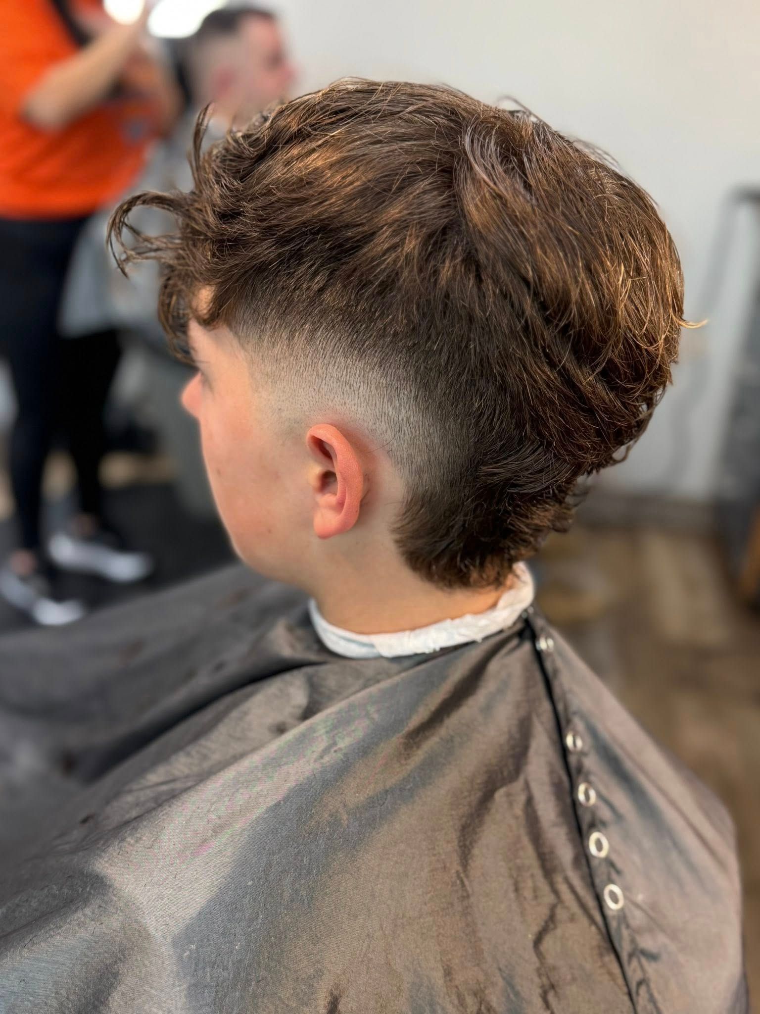 Person with a curly undercut hairstyle in a barber chair, wearing a black cape during a haircut.