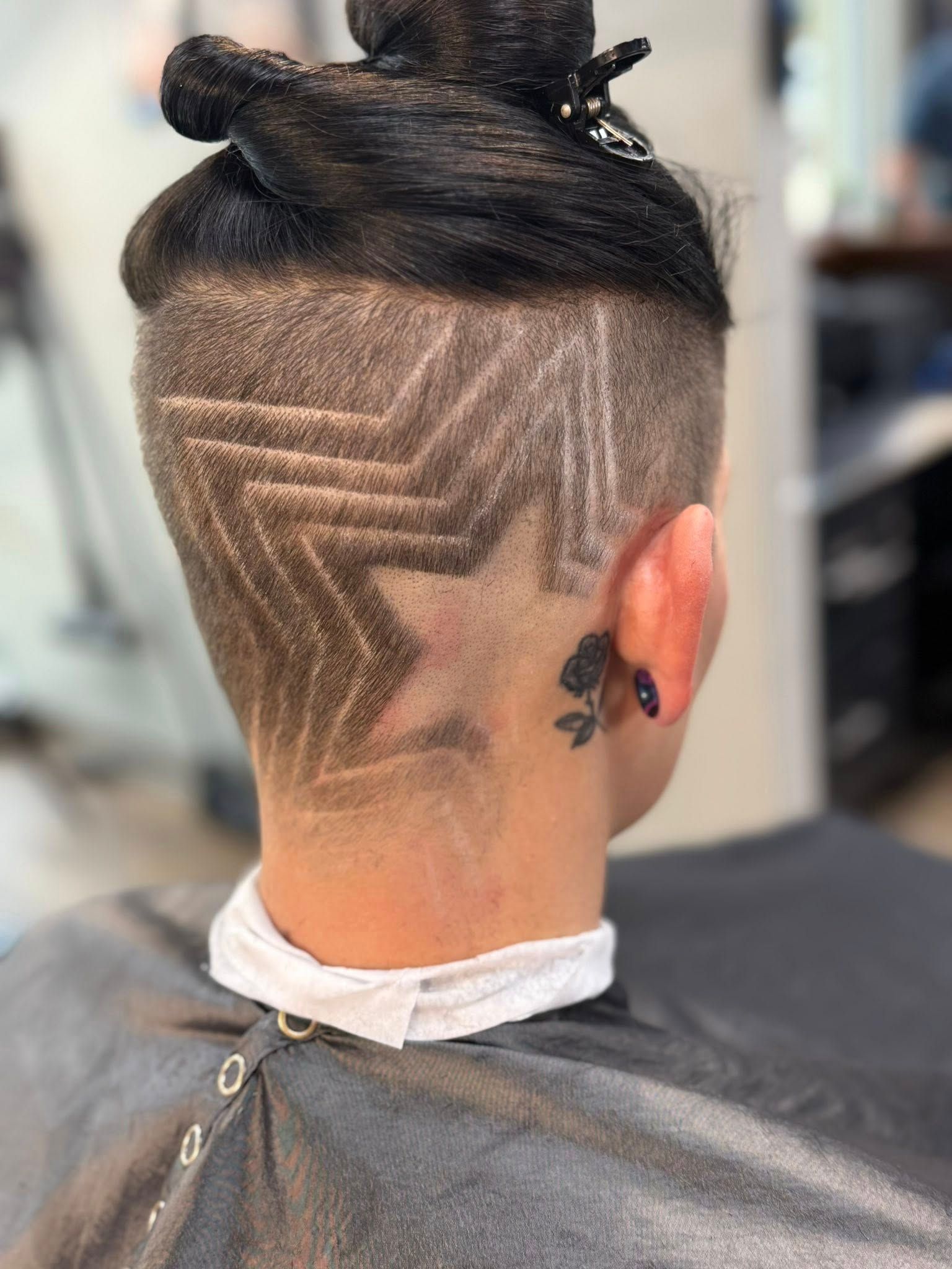 Back view of a head with geometric shaved hair design and a top bun in a barber chair