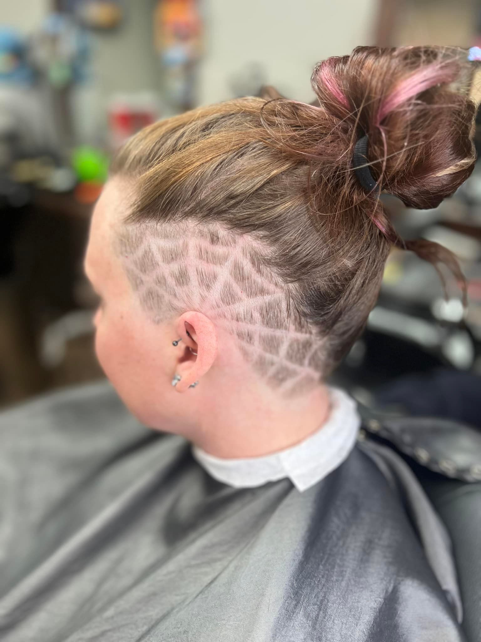 Side profile of a person with a braided bun and shaved patterned undercut at a salon.