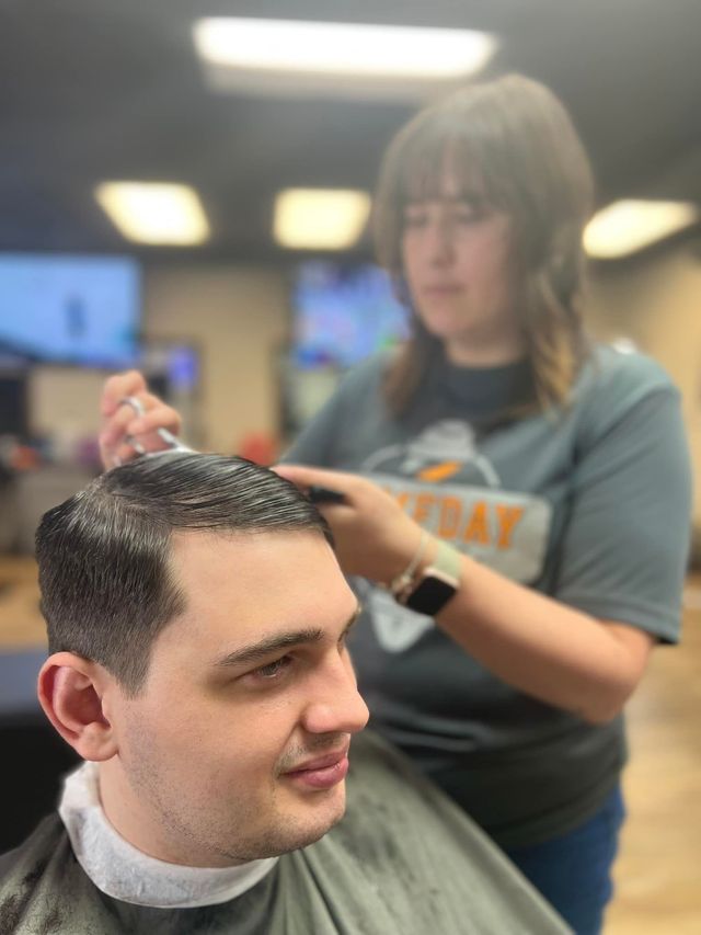 Barber giving a man a haircut indoors. The man smiles while the barber works.