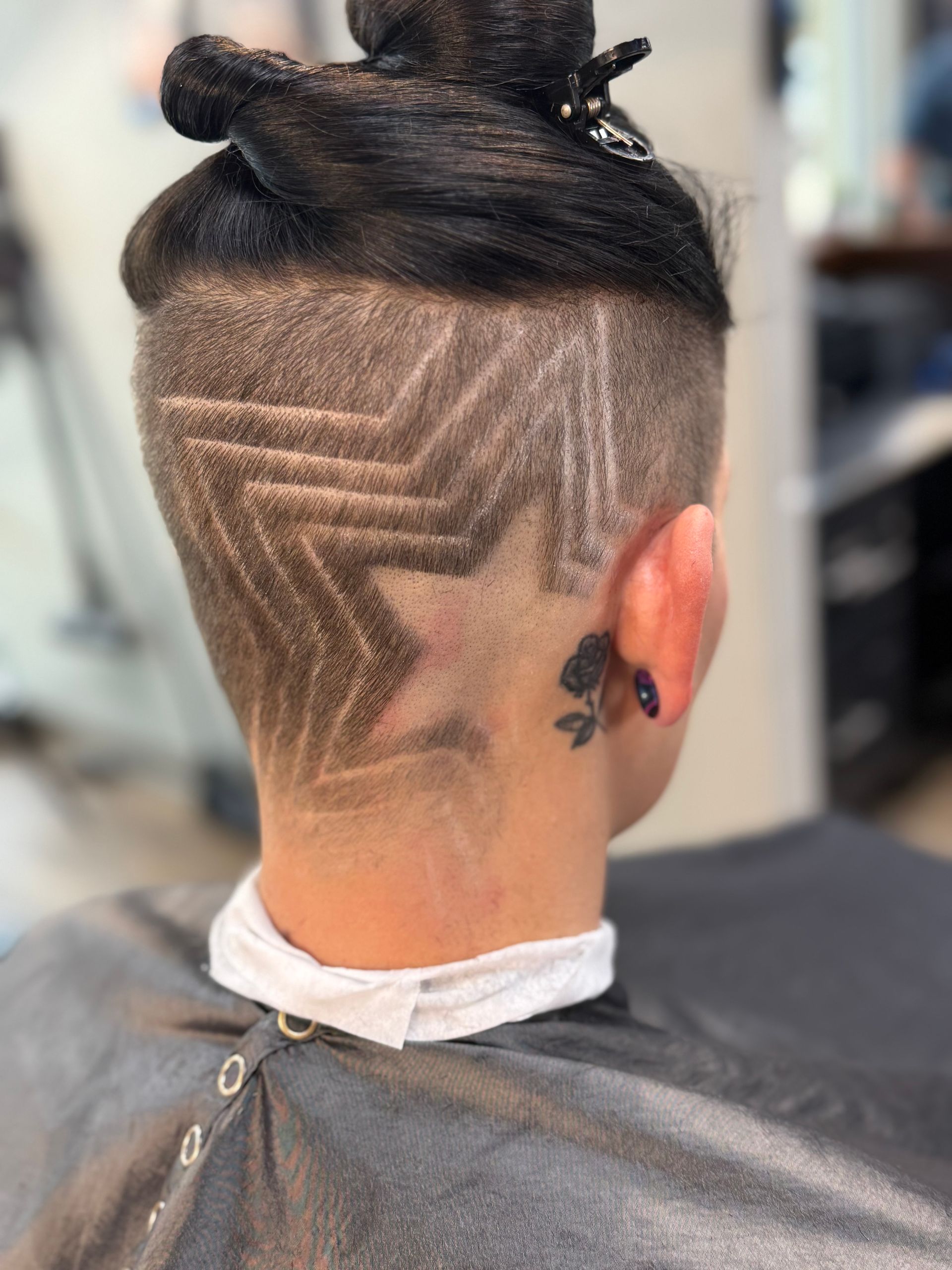 Undercut hairstyle with geometric shaved pattern and a top bun, viewed from the back.
