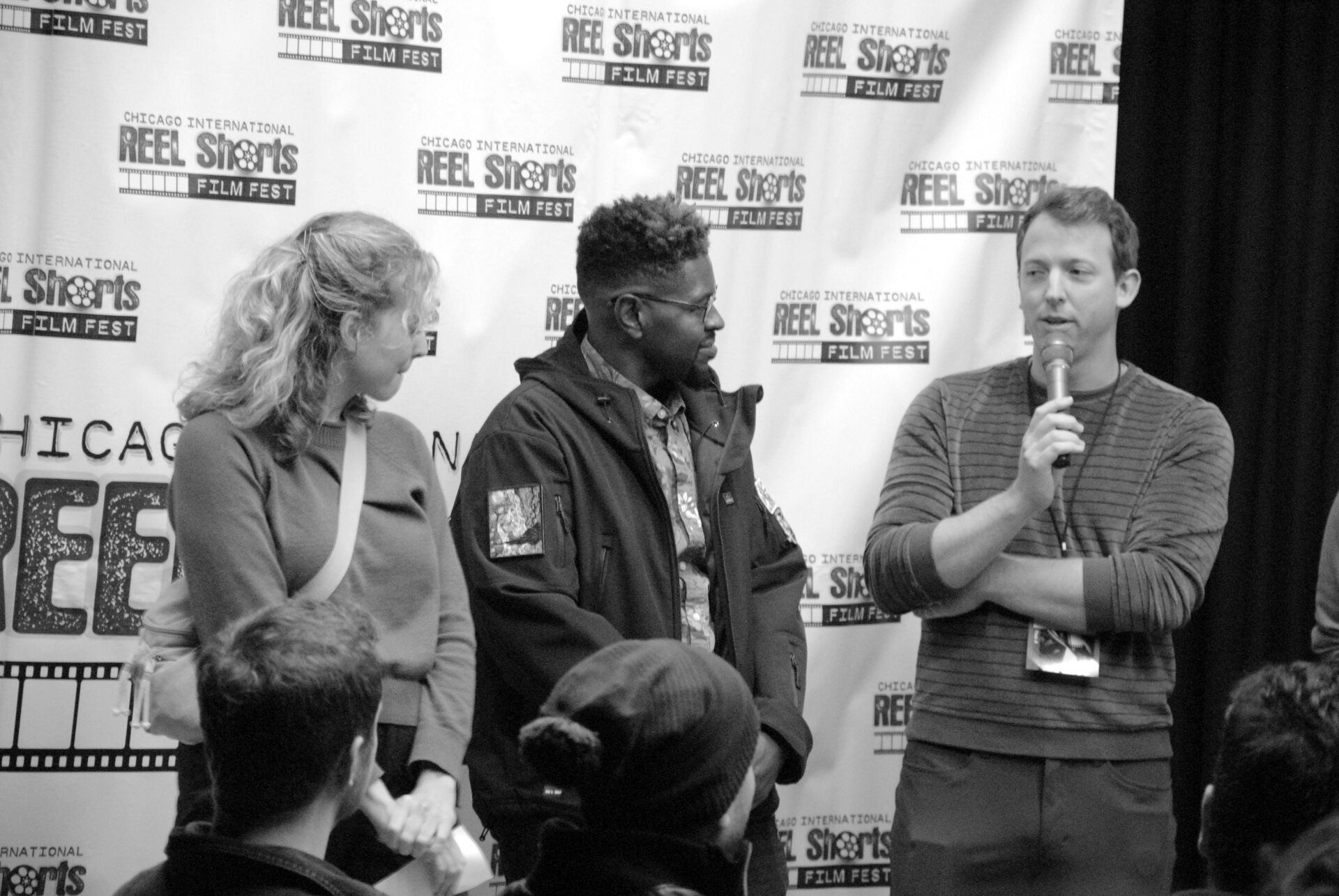 Three people at a film festival event, one speaking into a mic. Chicago REEL Shorts backdrop.
