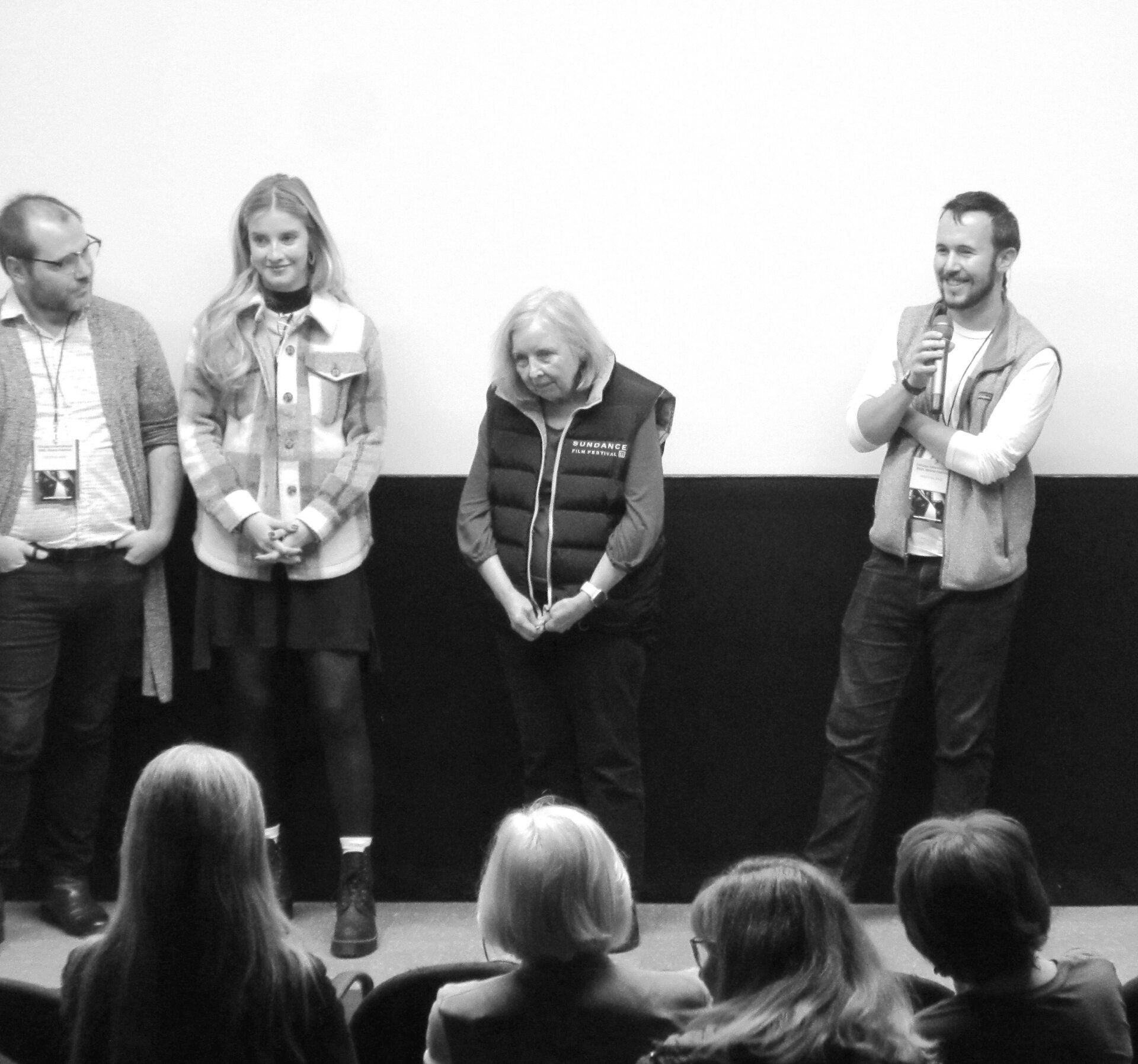 Panel of four people on stage; audience seated below.