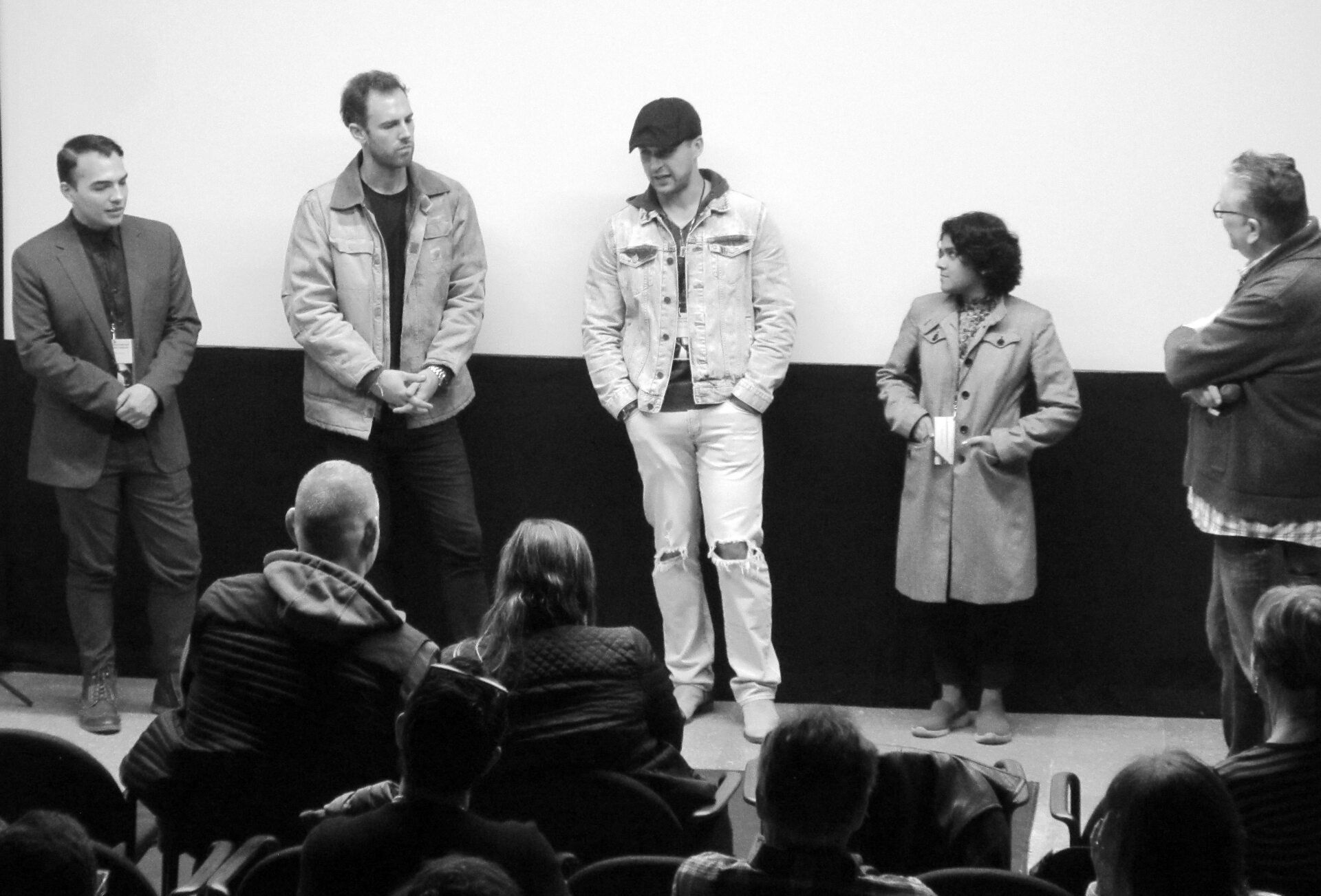 Panel of speakers on a stage, facing an audience in a theater setting. Black and white photo.