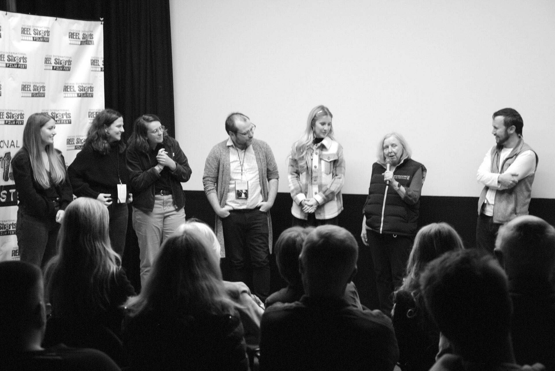 Group on stage at a film festival, facing audience, with microphone. Black and white photo.