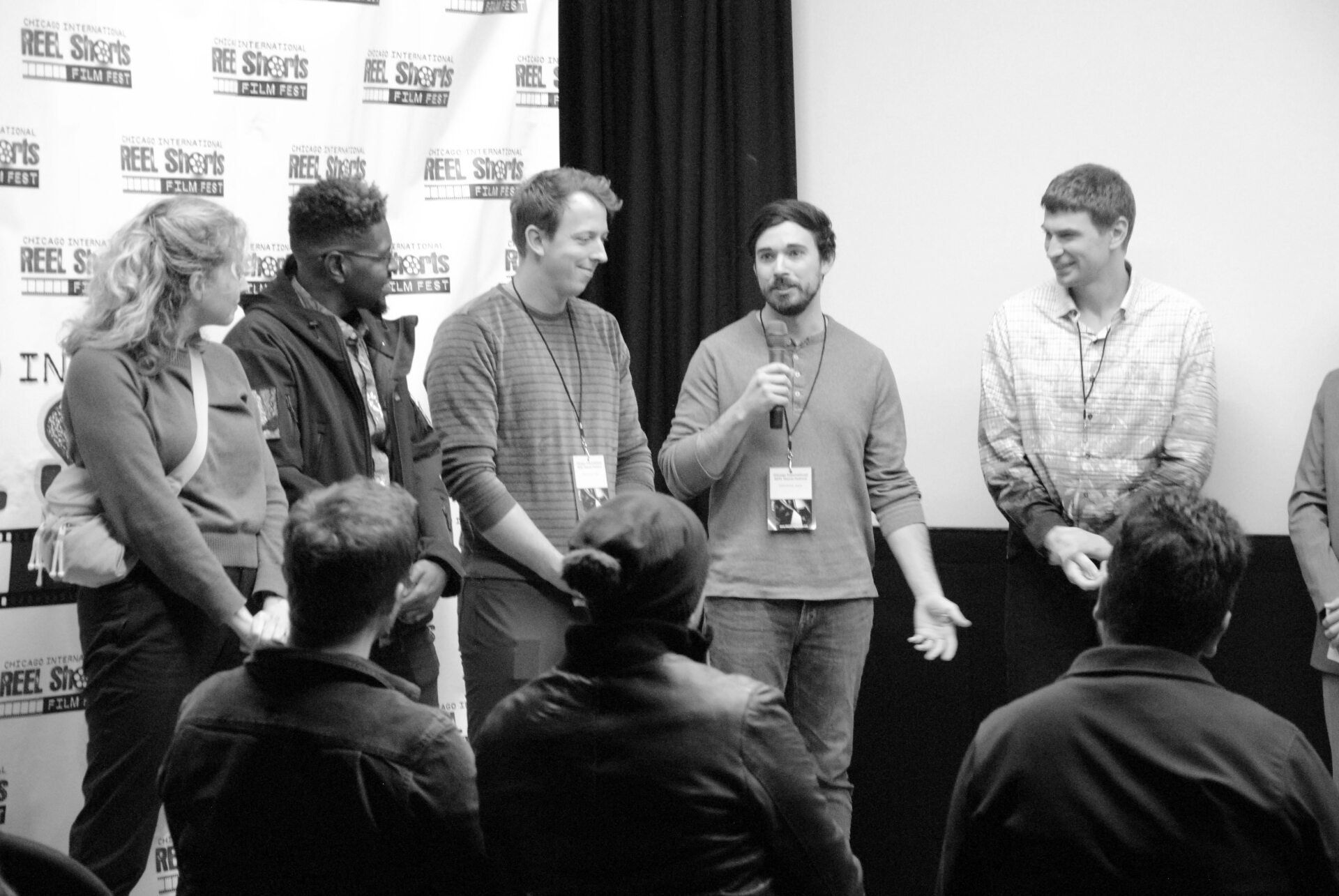 Panel of six people on stage, speaking to audience. Black and white photo.