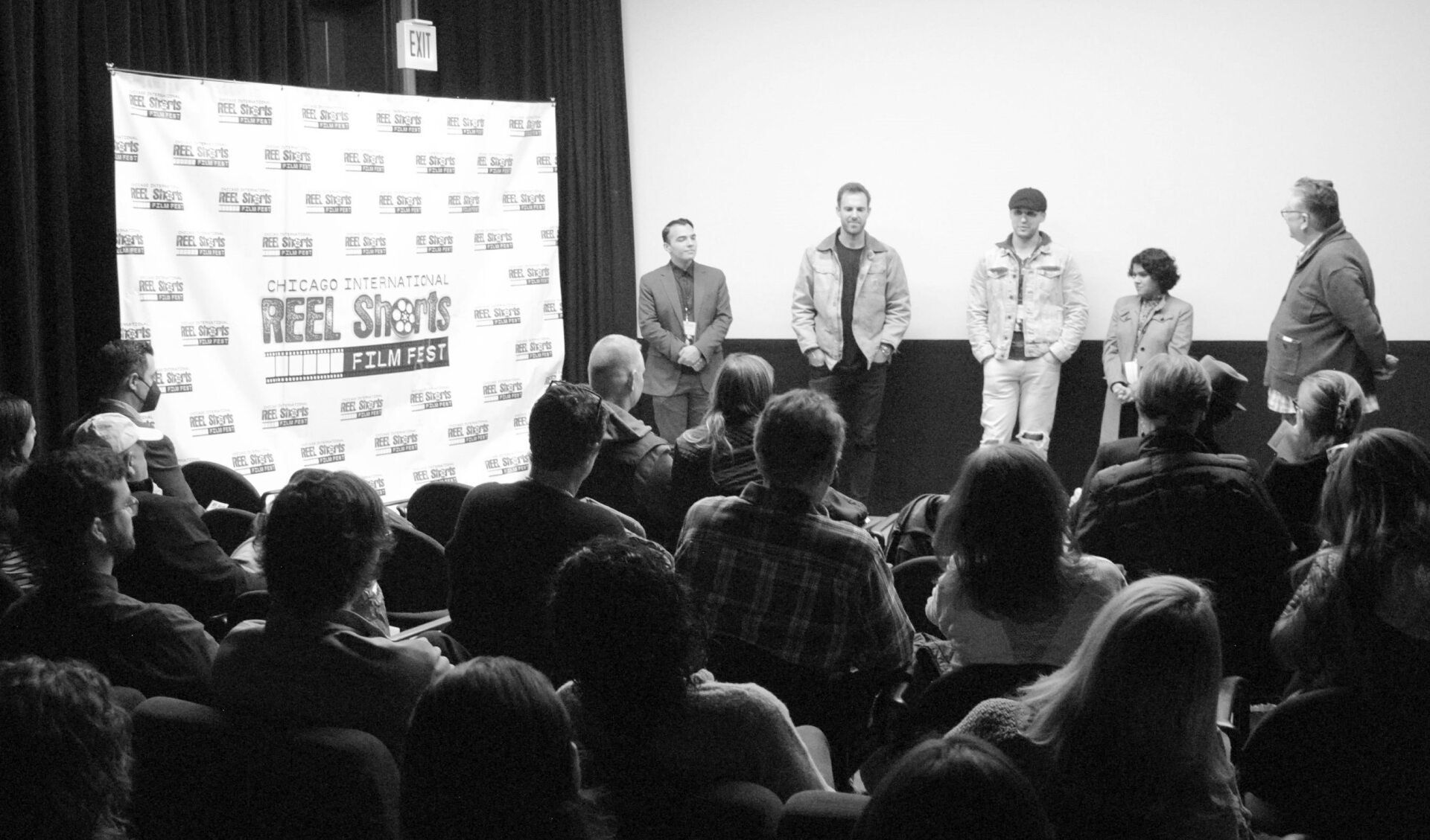 Panel discussion with filmmakers onstage, addressing an audience seated in a theater. Black and white.