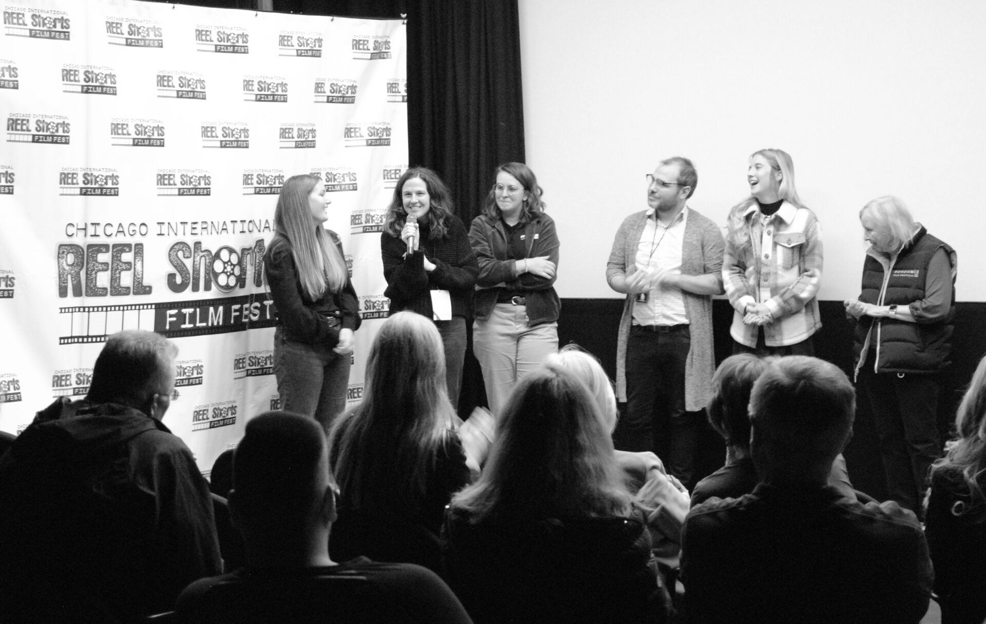 Group of people on stage, possibly filmmakers, at a film festival Q&A. Black and white.
