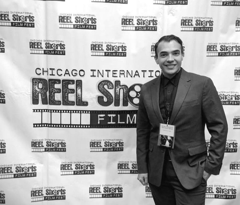 A man in a suit smiles at a film festival backdrop.